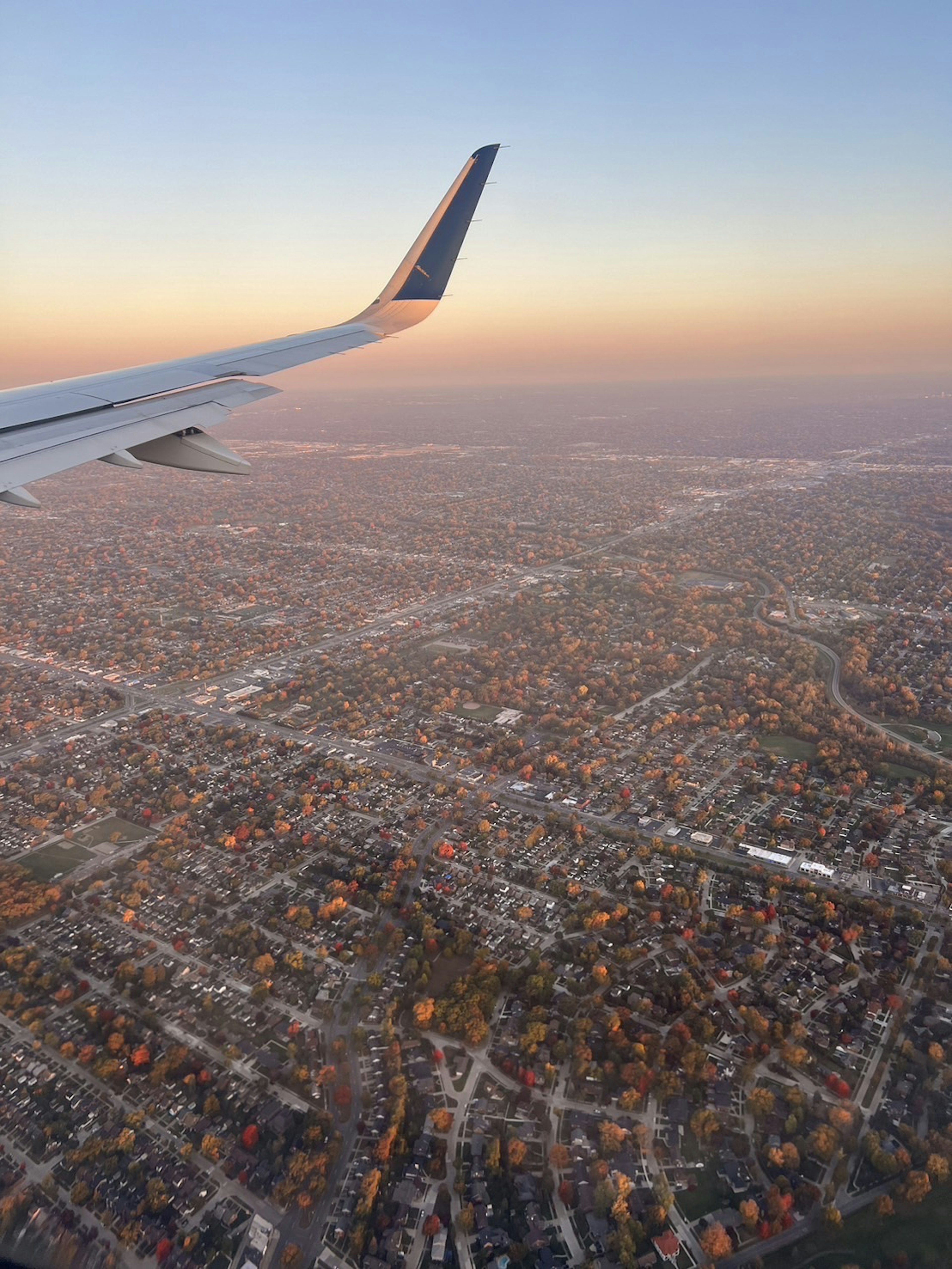 Flügel eines Flugzeugs mit Sonnenuntergang über einer Stadtlandschaft