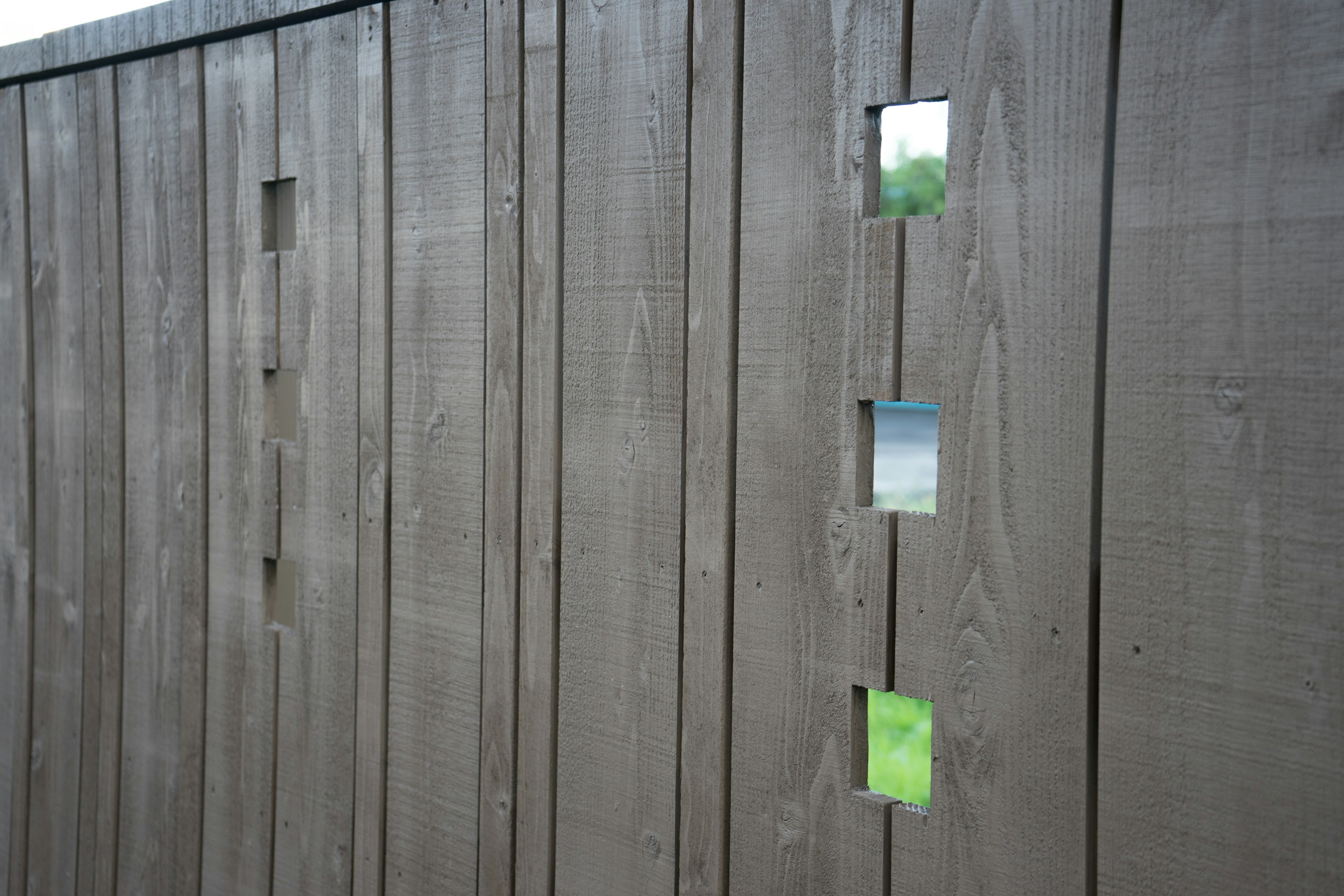 Image of a wooden fence with vertical planks featuring square cutouts