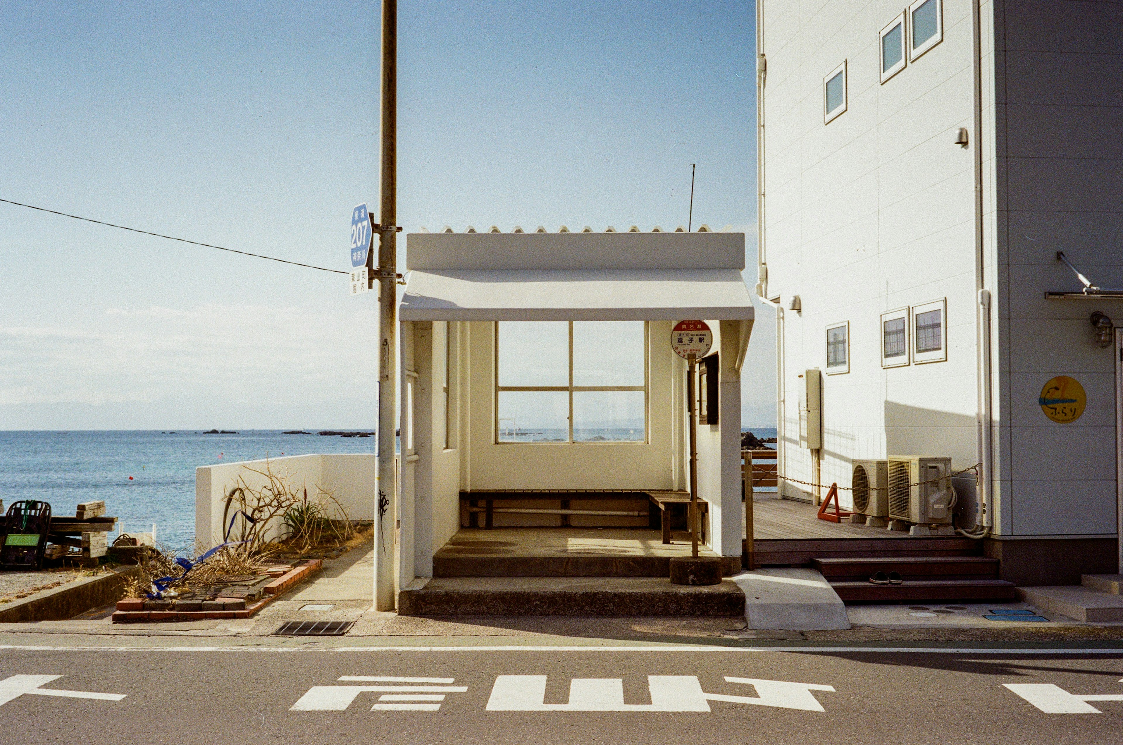 White bus stop near the ocean with a building in the background