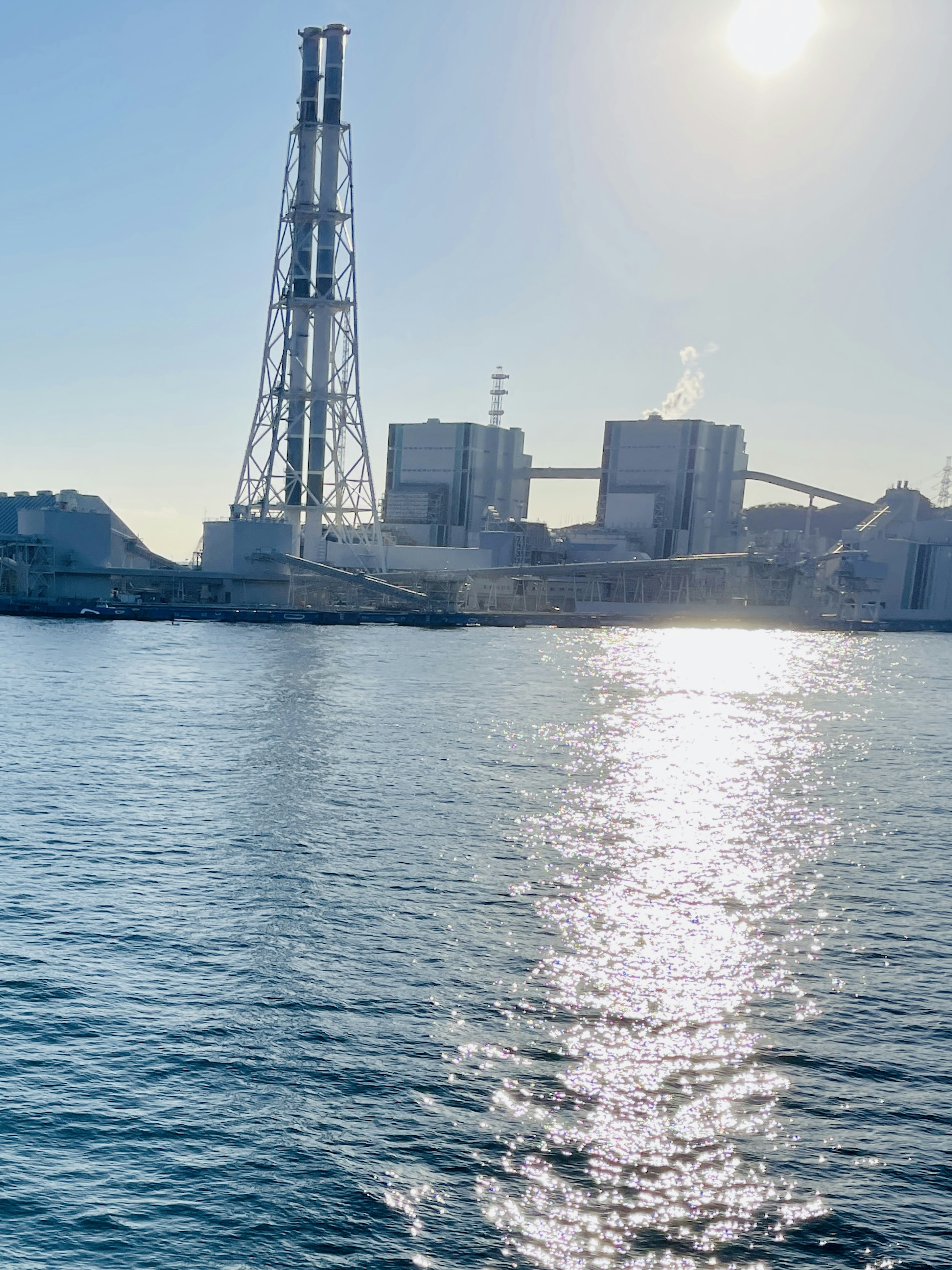 Silhouette einer Industrieanlage, die im Wasser mit Sonnenlicht reflektiert wird