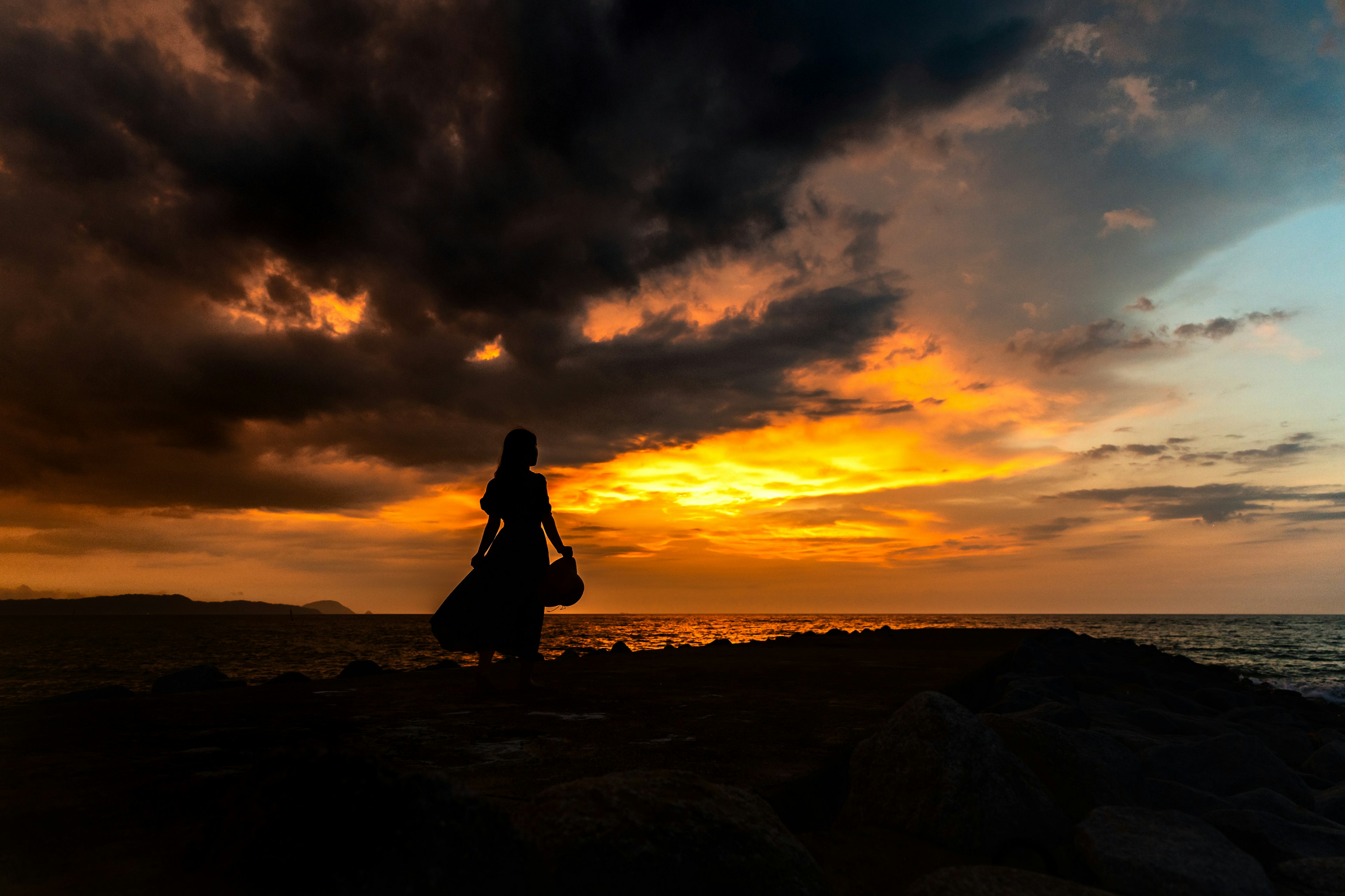 夕日の中でシルエットの人物が海岸に立っている風景