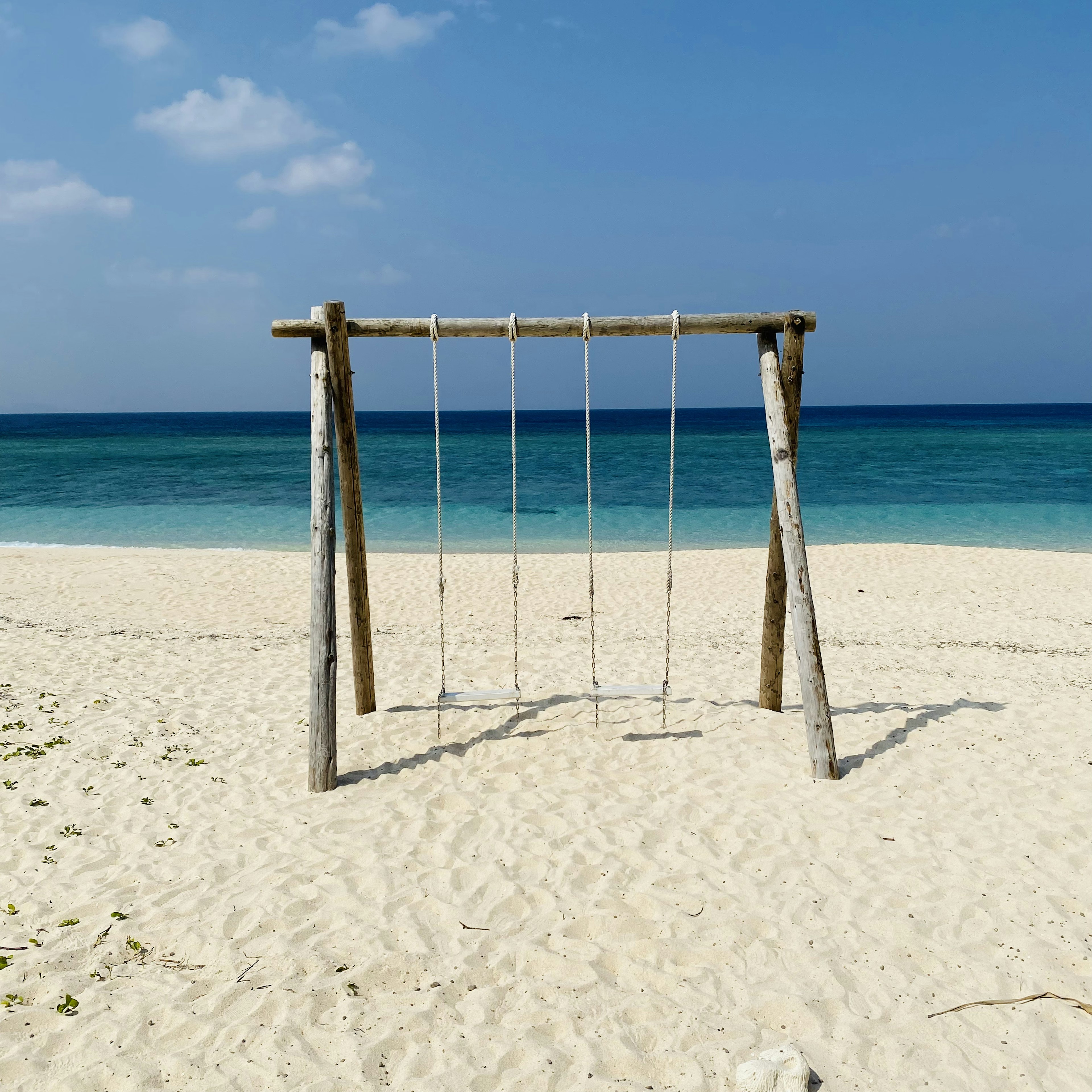 Wooden swing set on a white sandy beach with blue ocean background