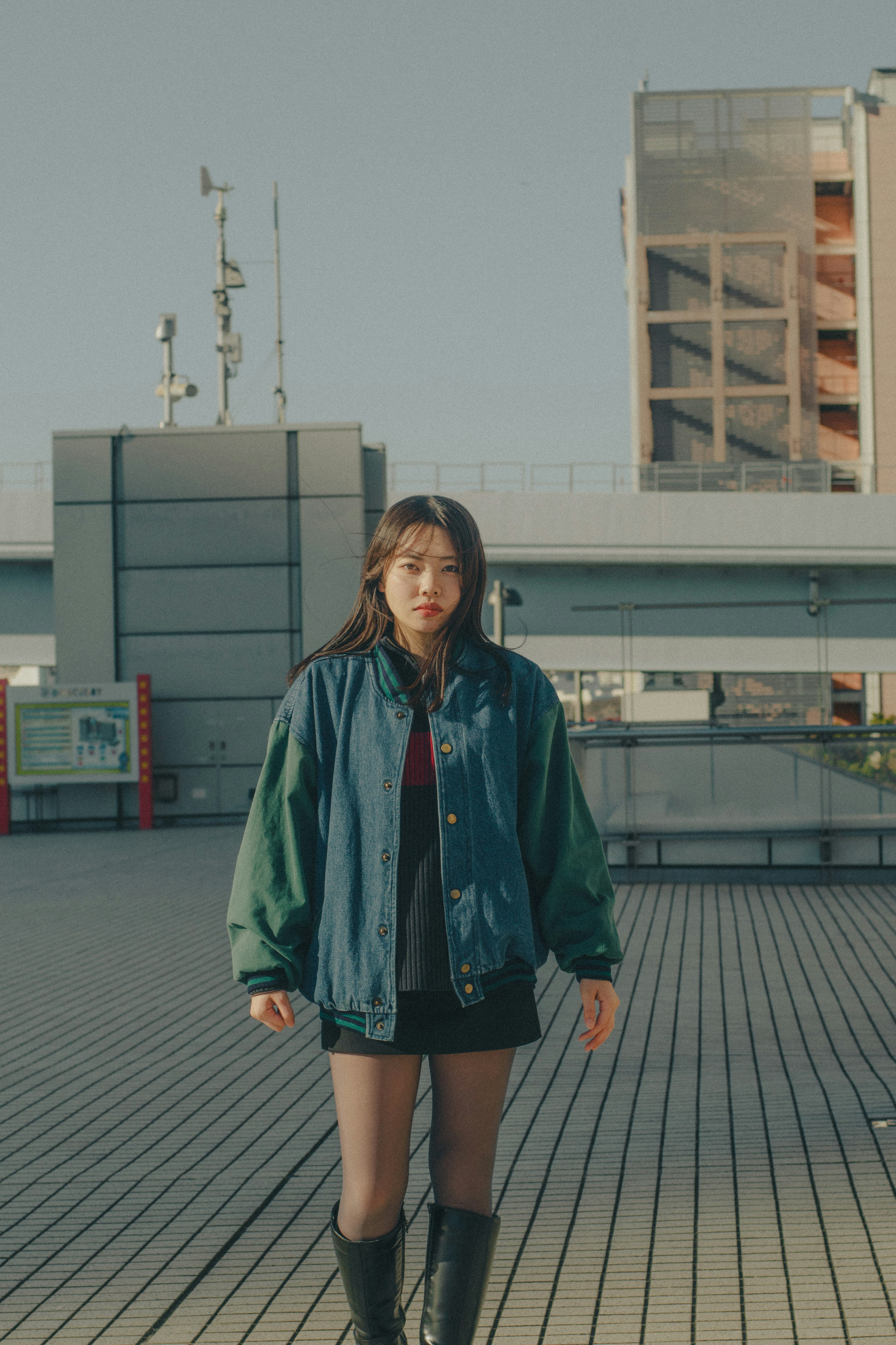 A woman standing outdoors in a casual street-style outfit featuring a green and blue jacket and a black skirt