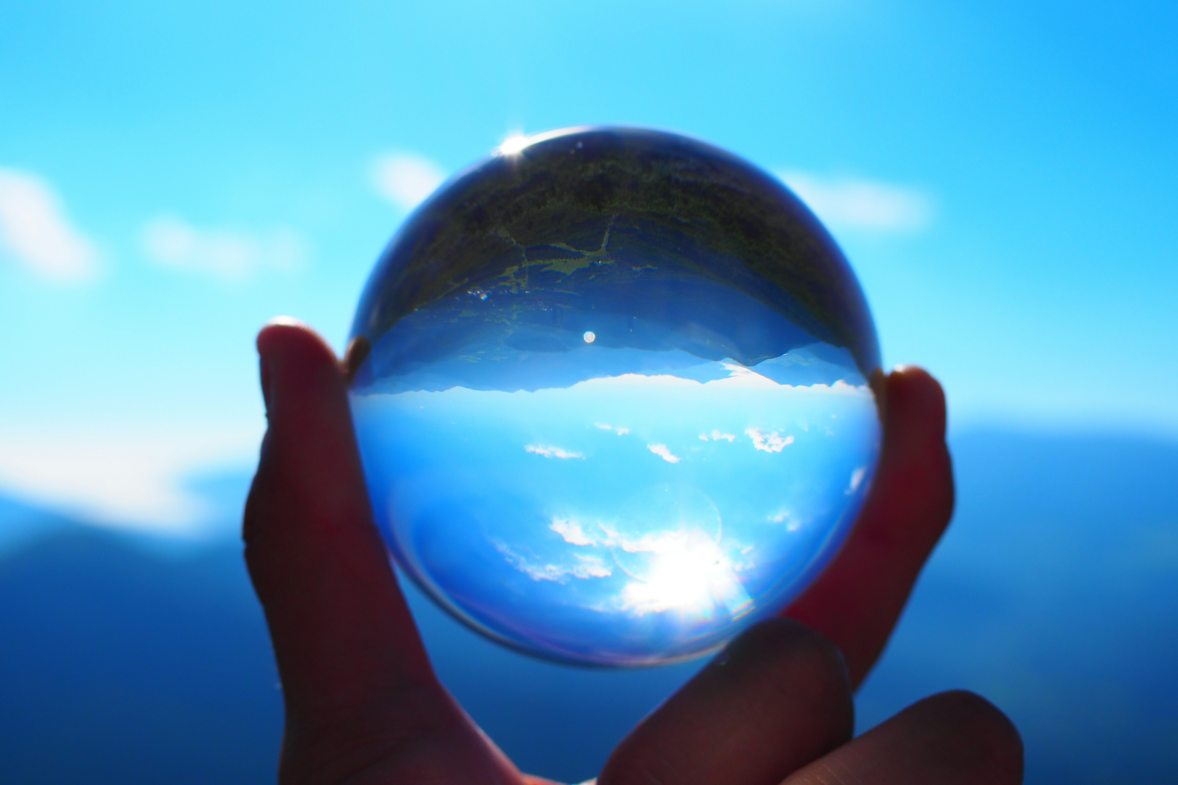 A person holding a crystal ball reflecting a blue sky and mountains