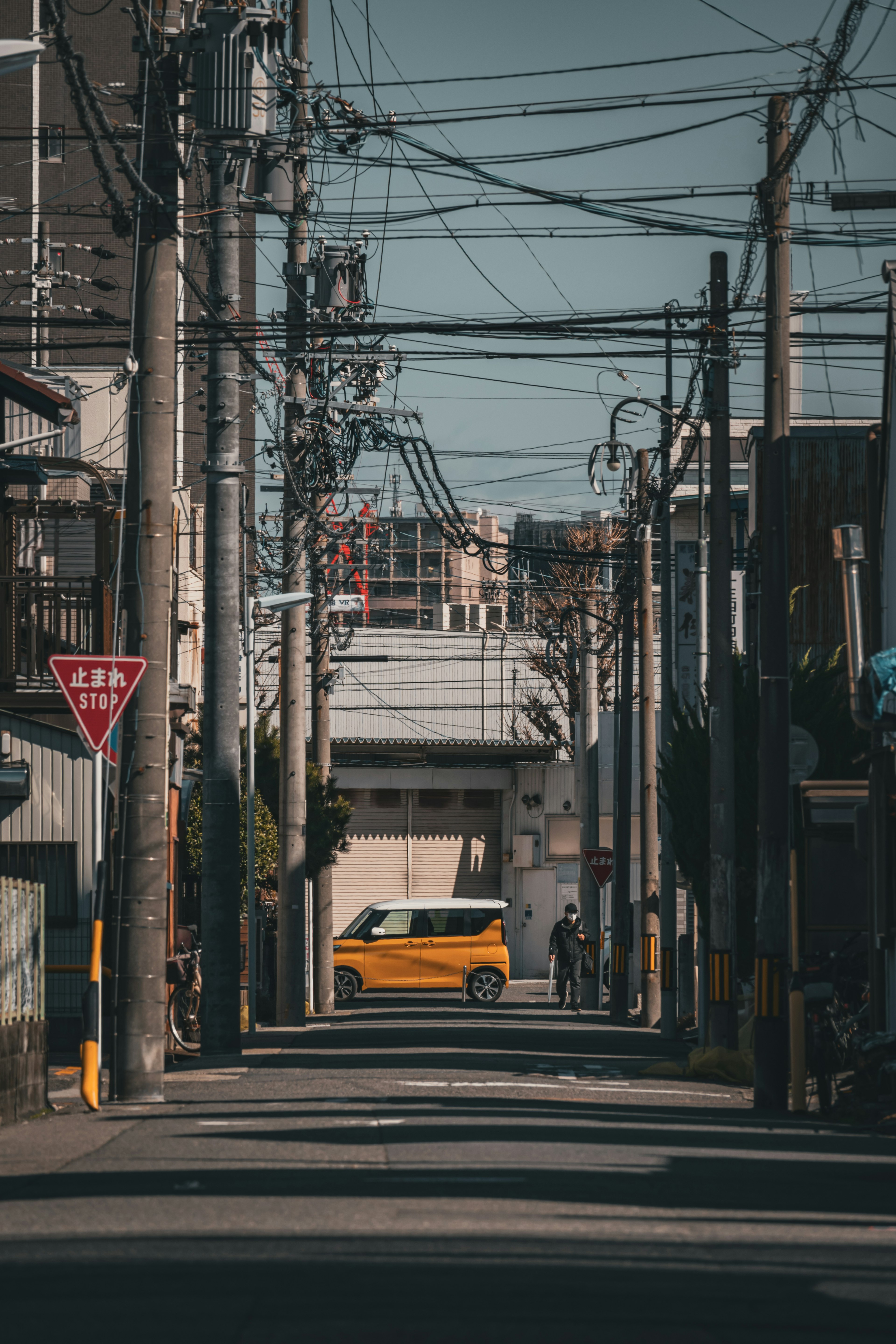 狭い路地に黄色い車が停まっている街の風景 電線が交差する