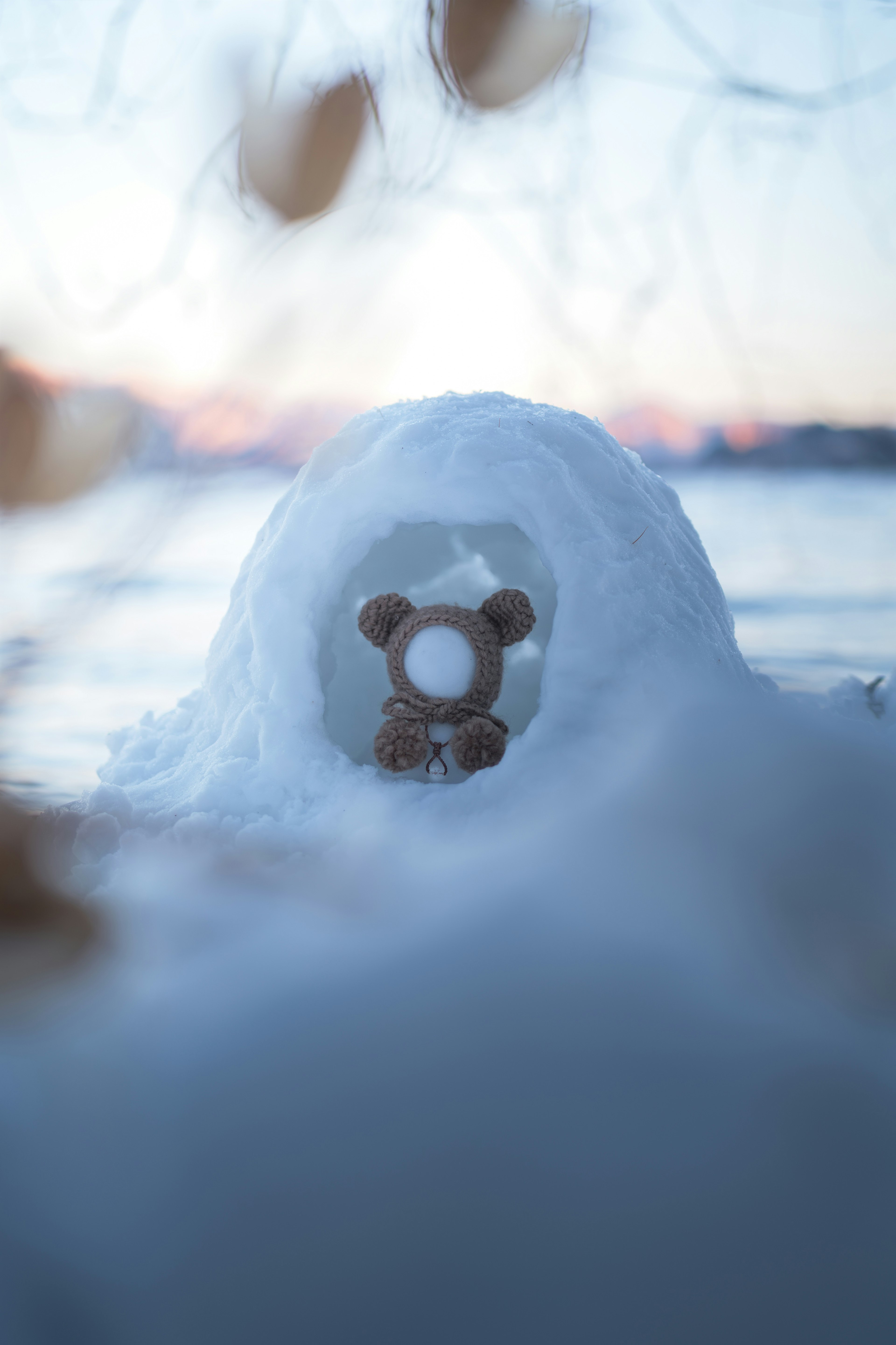 Un piccolo igloo di neve con un orsetto di peluche marrone seduto davanti