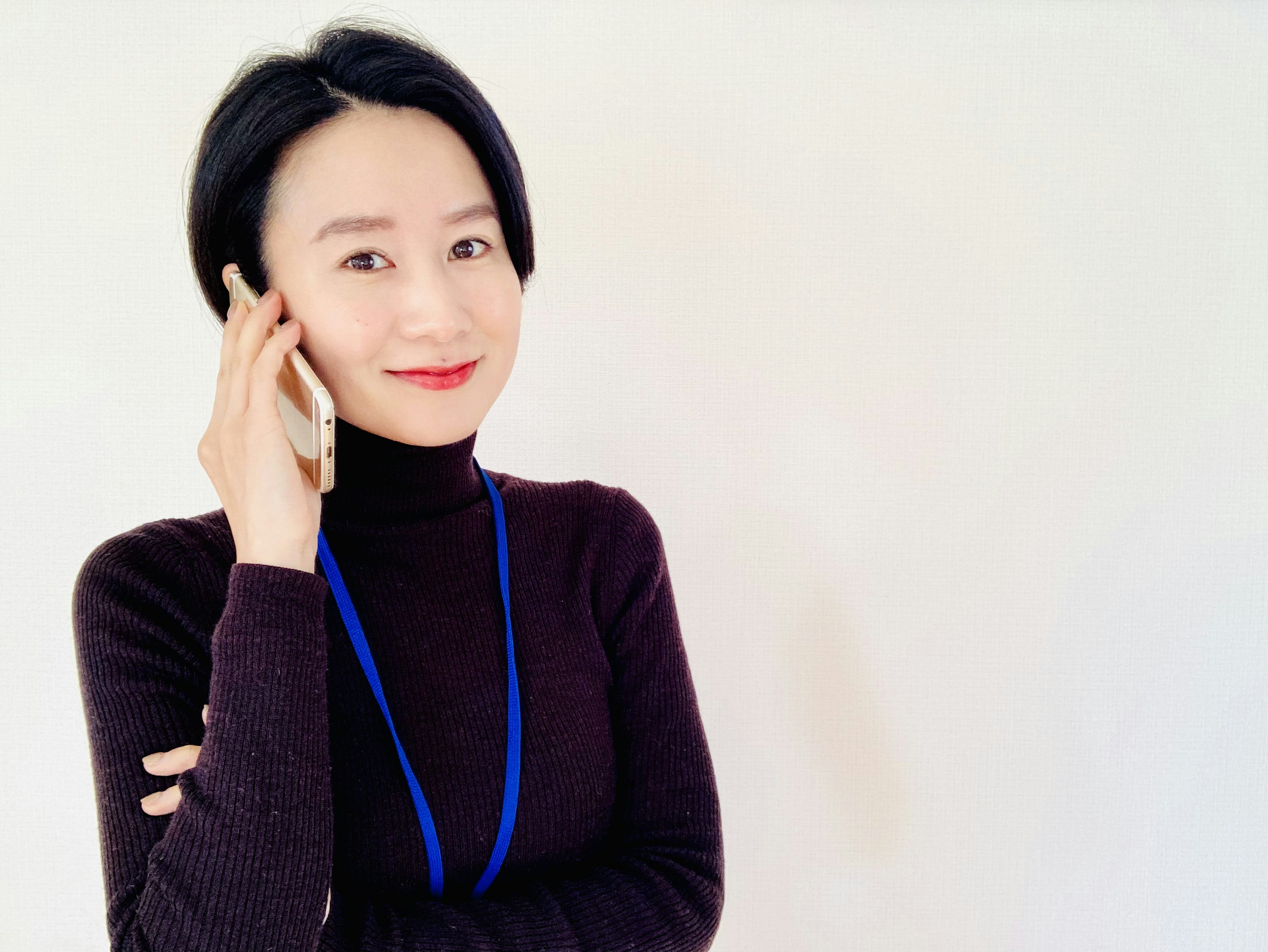 Portrait of a woman on the phone wearing a black turtleneck and blue lanyard with a confident smile