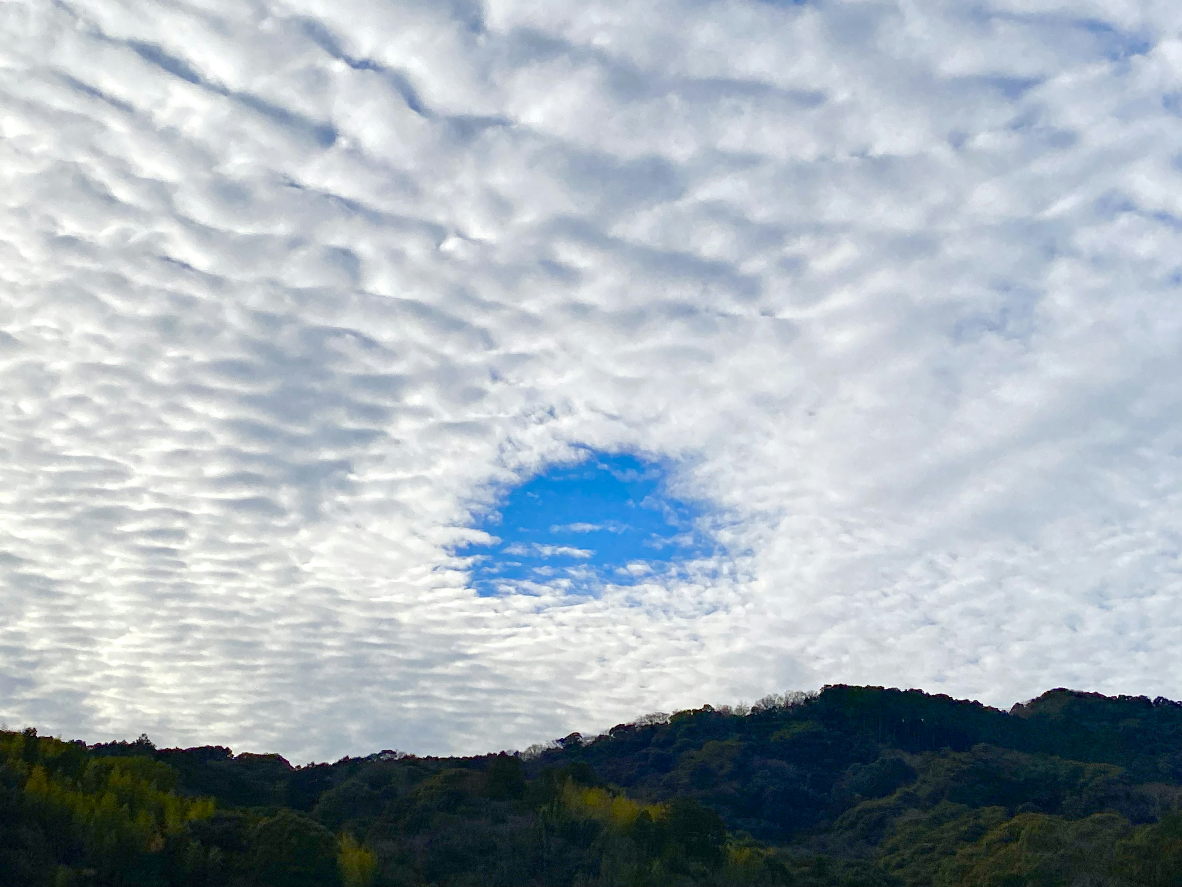 Ciel avec un trou dans les nuages révélant le bleu et des montagnes en dessous