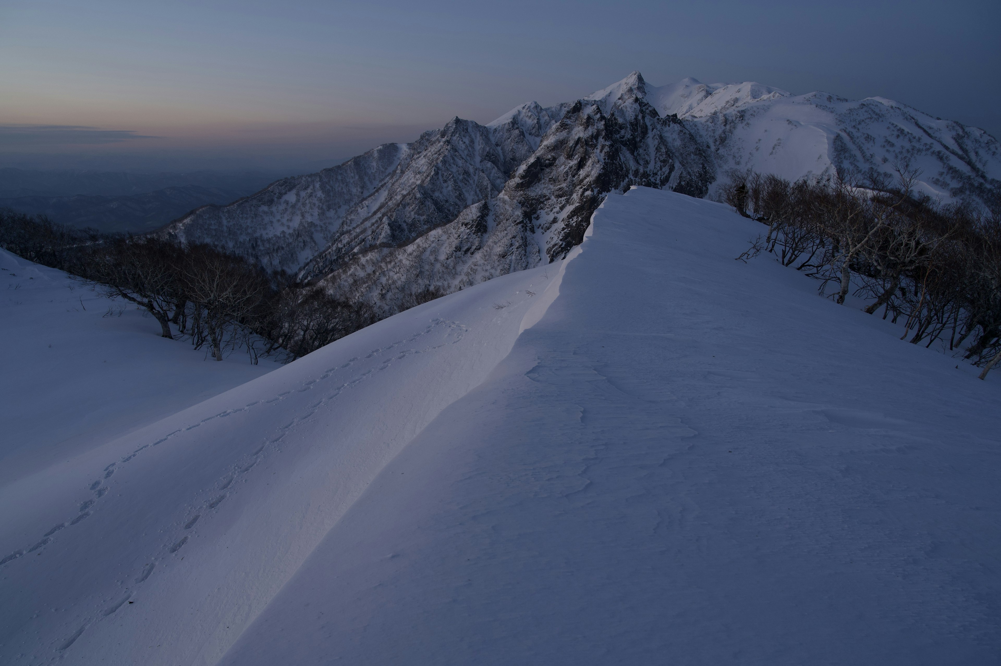 Chaîne de montagnes enneigée sous un ciel crépusculaire