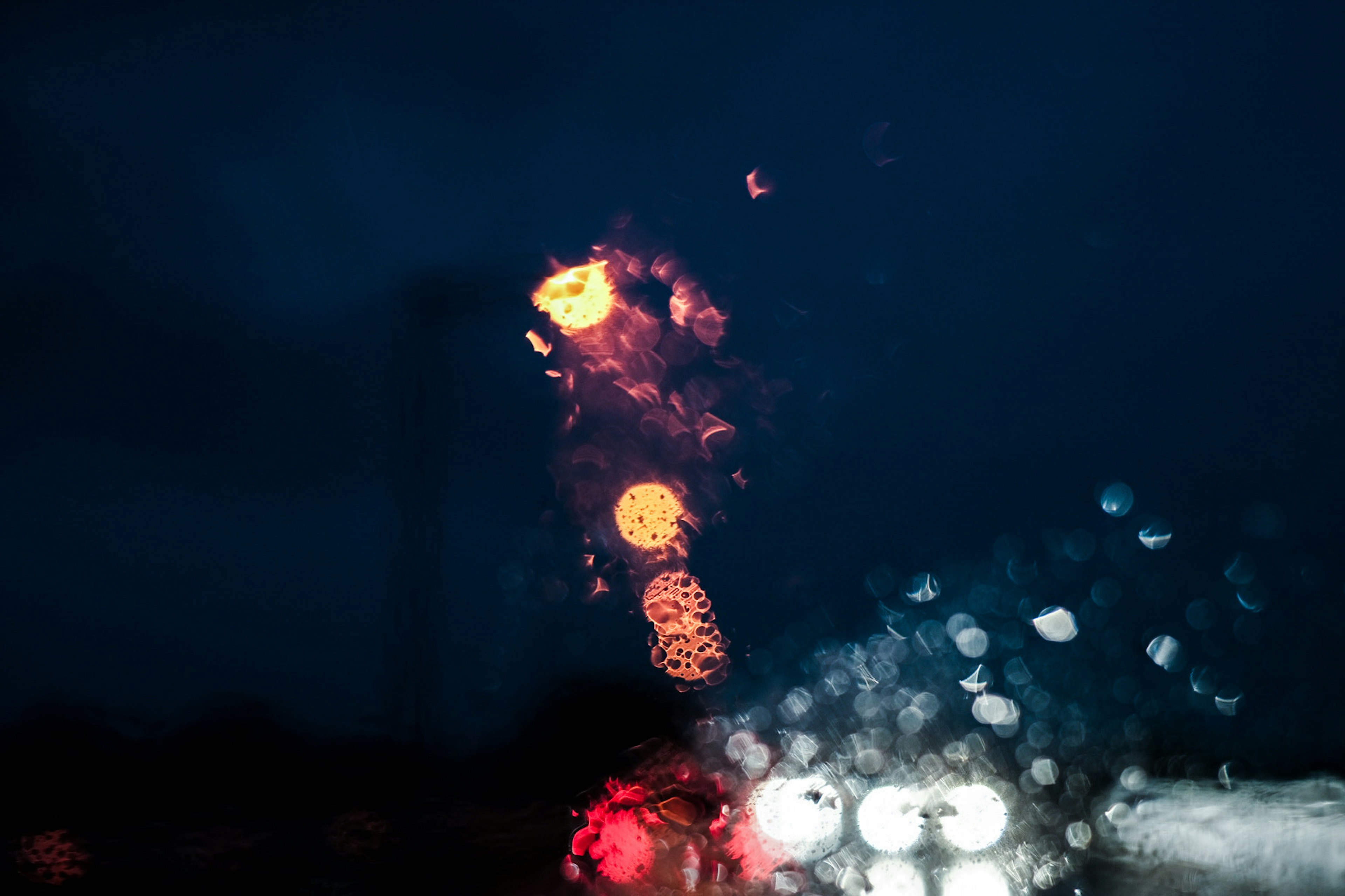 Gotas de lluvia en una ventana con luces borrosas en un entorno oscuro