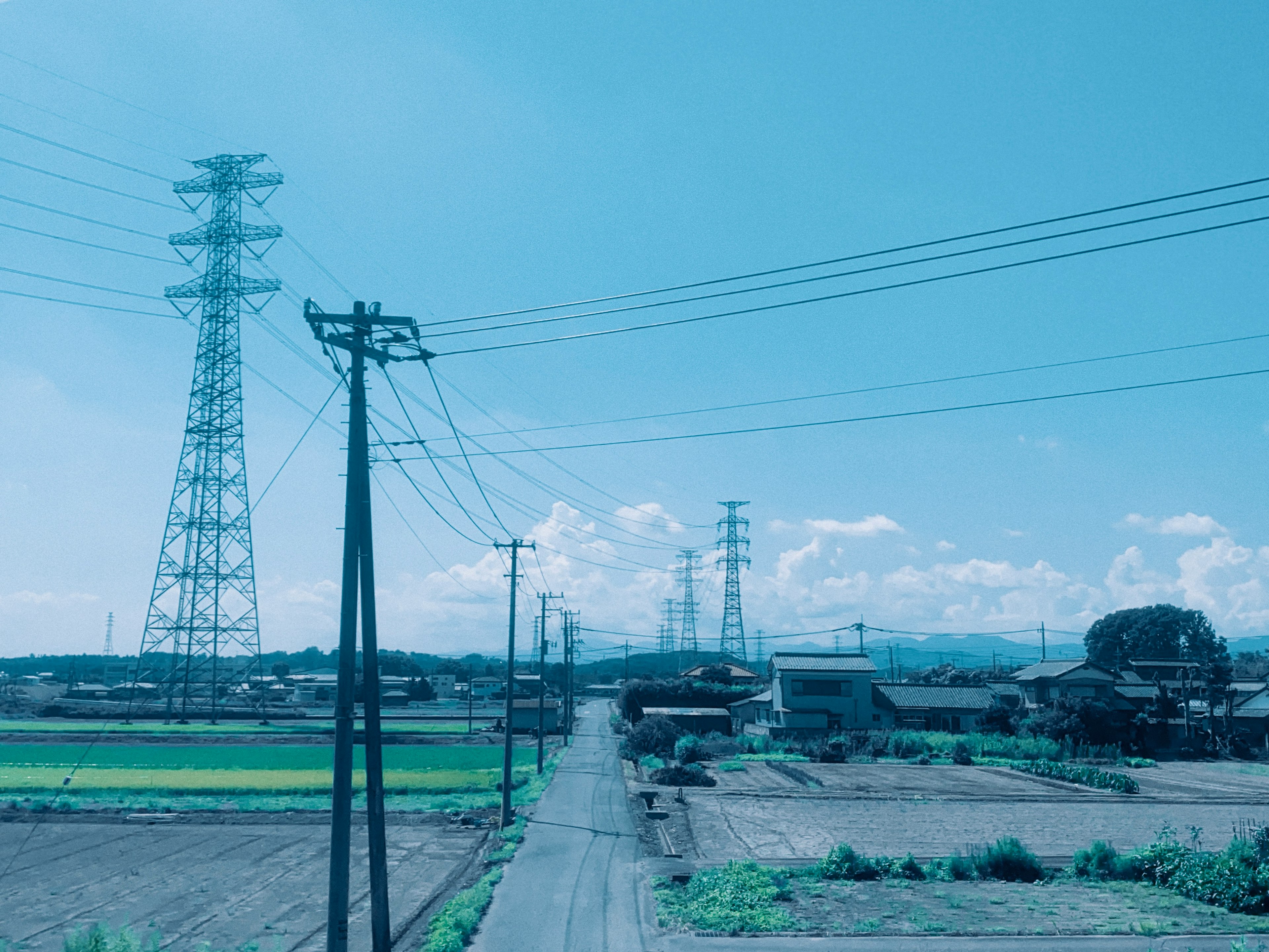 Paisaje rural bajo un cielo azul con postes de servicio y líneas eléctricas a lo largo de un camino rural