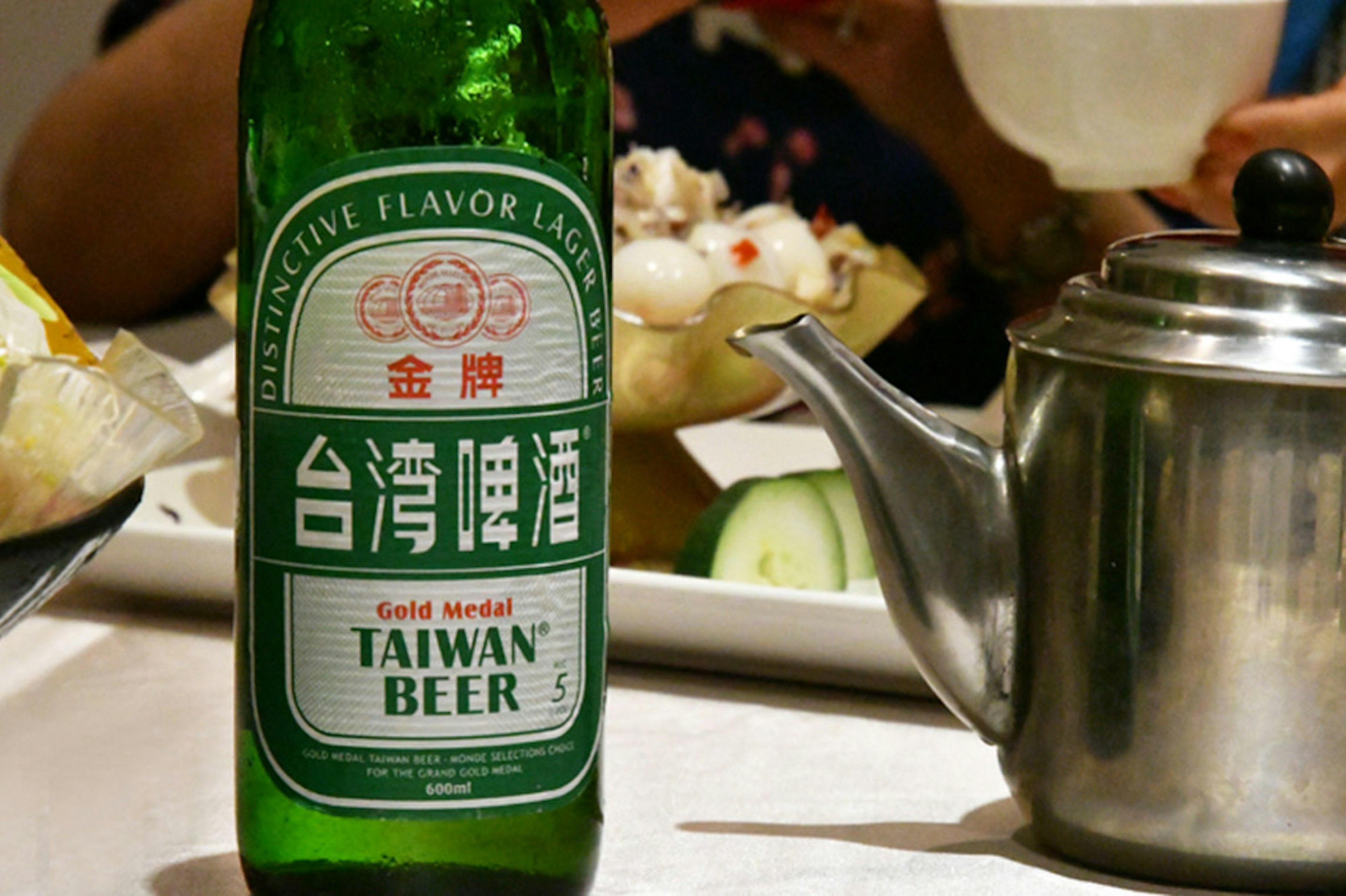 Eine grüne Flasche Taiwan Bier und eine Teekanne auf einem Esstisch