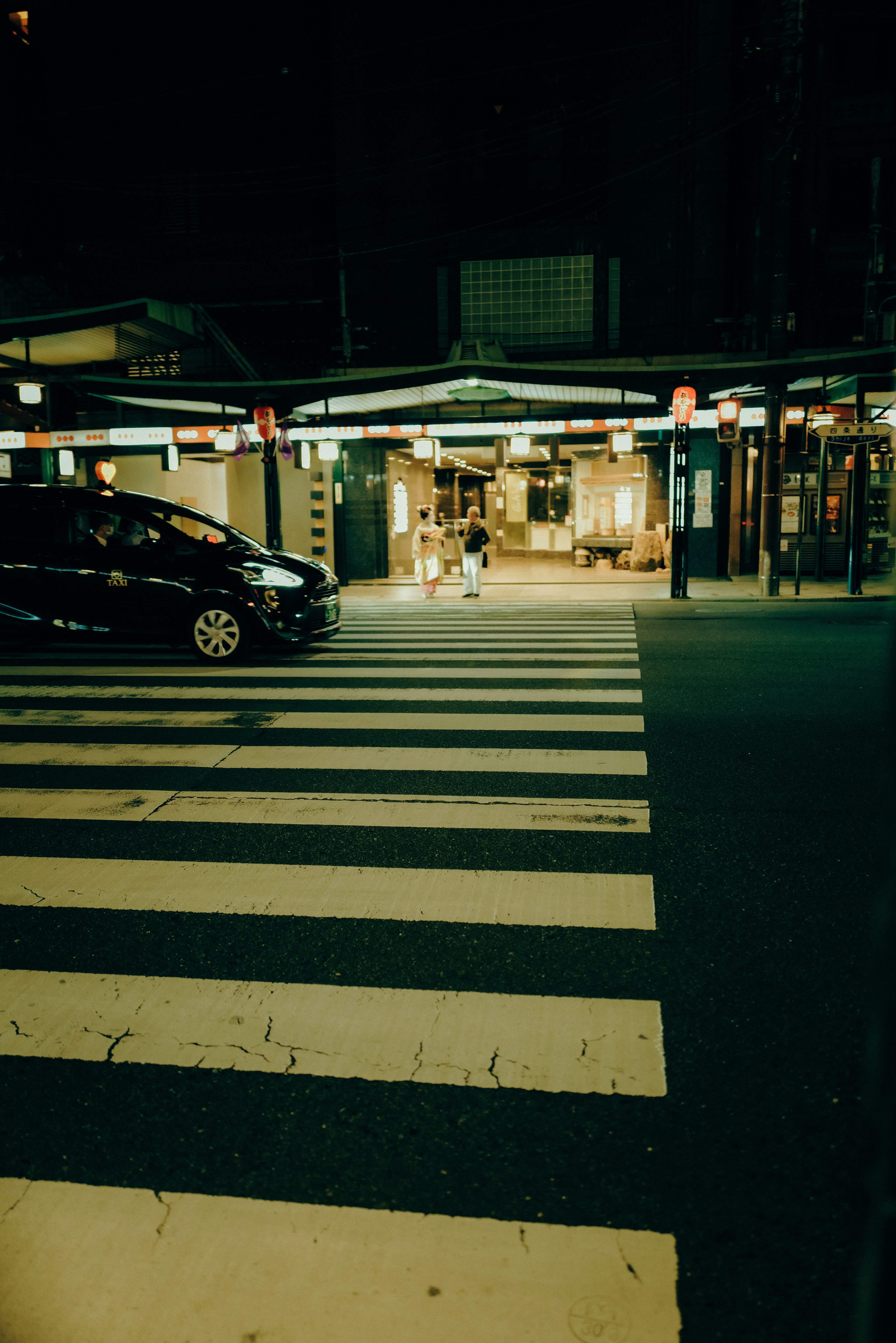 Nighttime street scene with a crosswalk and a black car