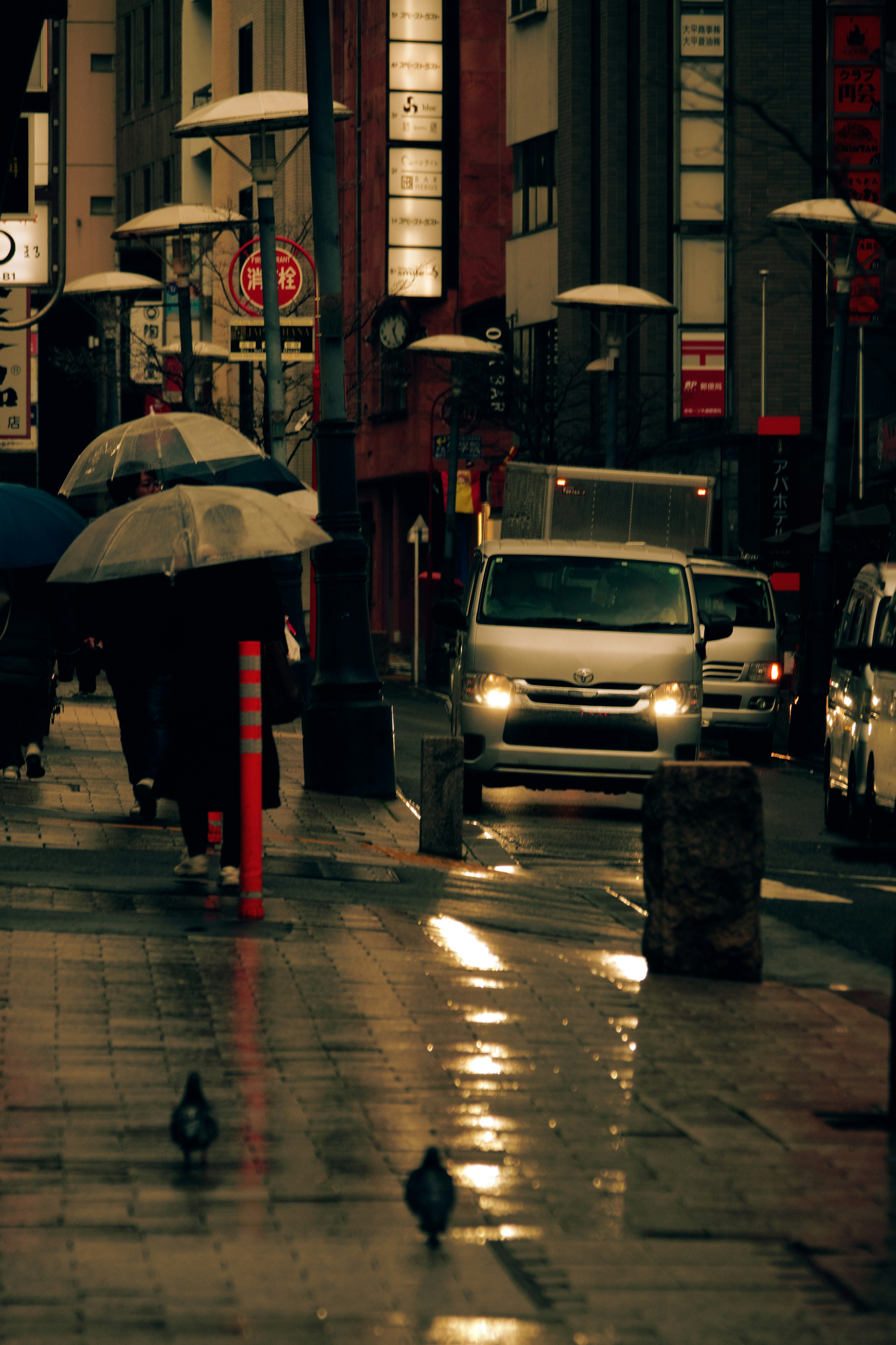 Scène de rue en ville avec des gens tenant des parapluies et une voiture qui passe sous la pluie