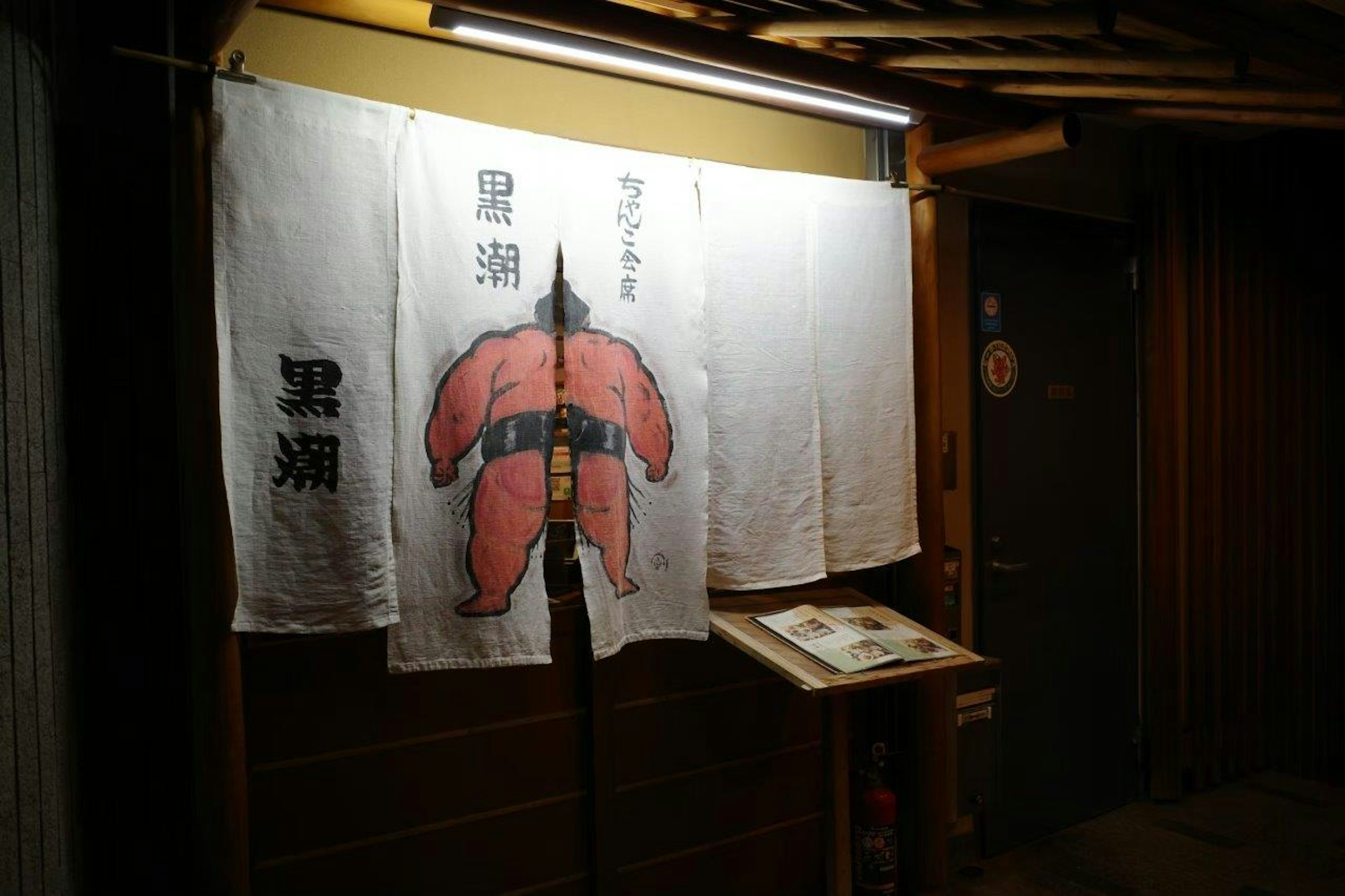 Entrance of a Japanese restaurant with a red sumo figure on a noren curtain