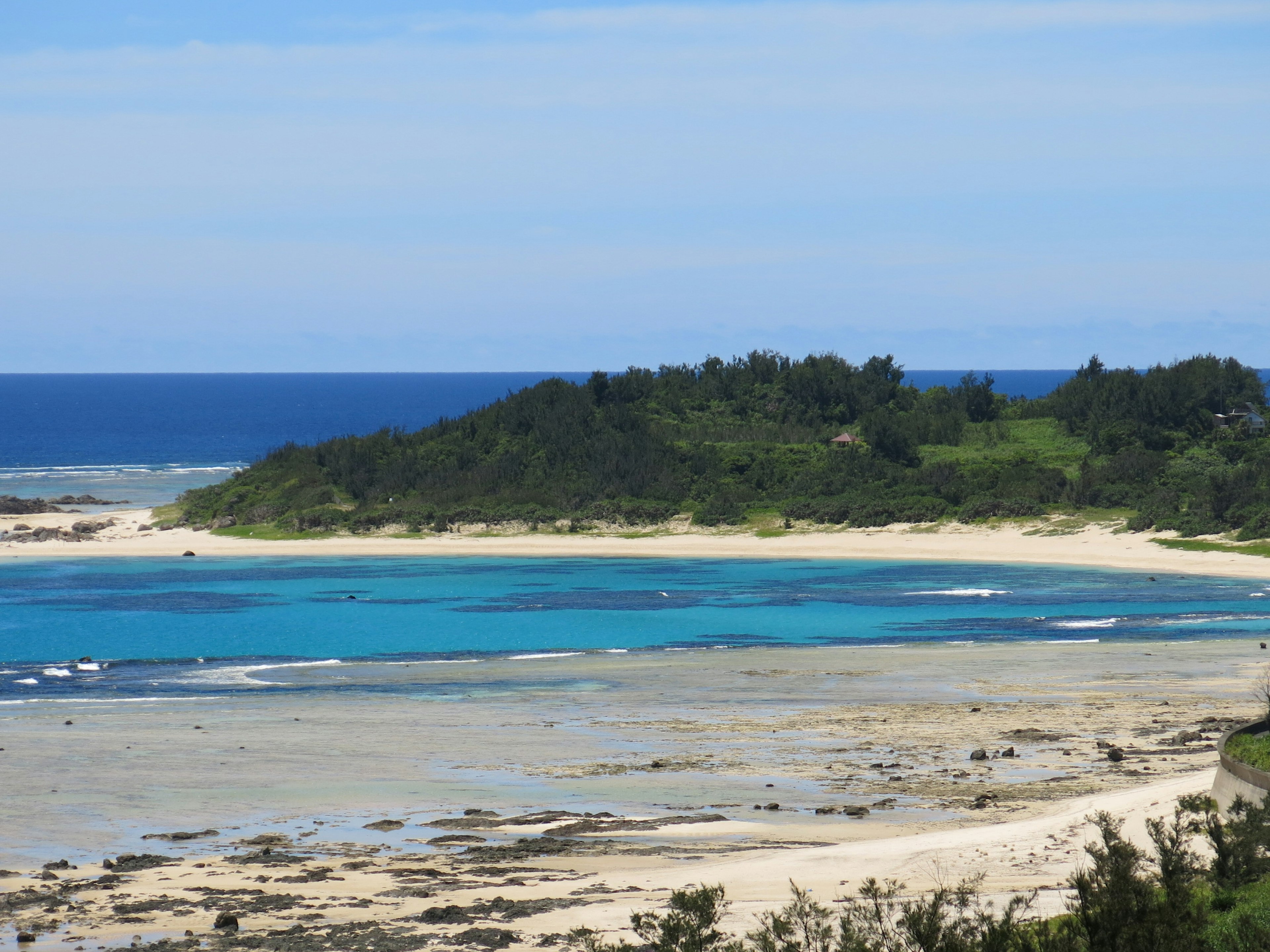 ทิวทัศน์ทะเลสีฟ้าและชายหาดทรายขาวมีเนินเขาสีเขียวอยู่เบื้องหลัง