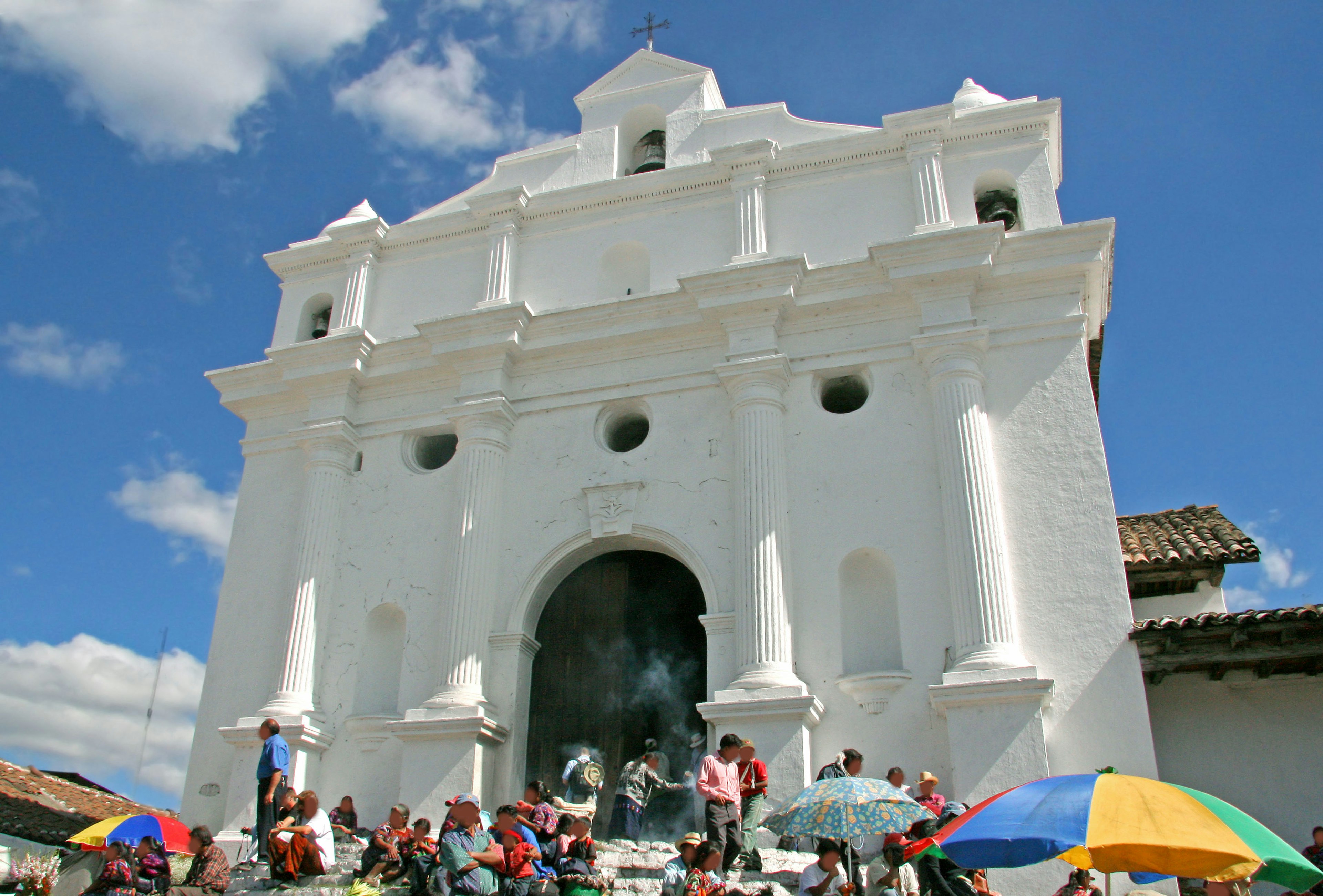 People gathering in front of a white church with colorful umbrellas