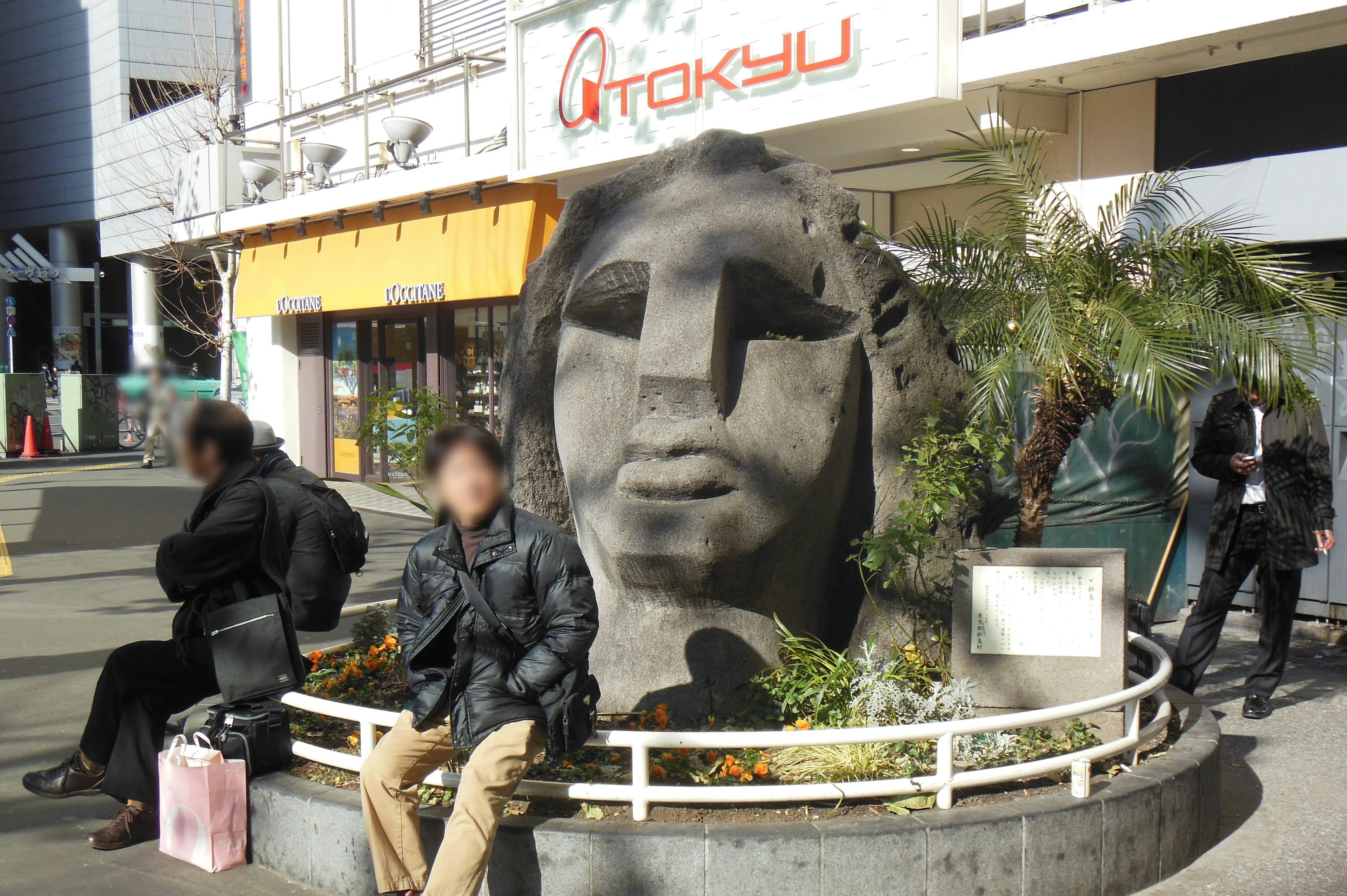 Grande sculpture en pierre dans un cadre urbain avec des personnes assises à proximité