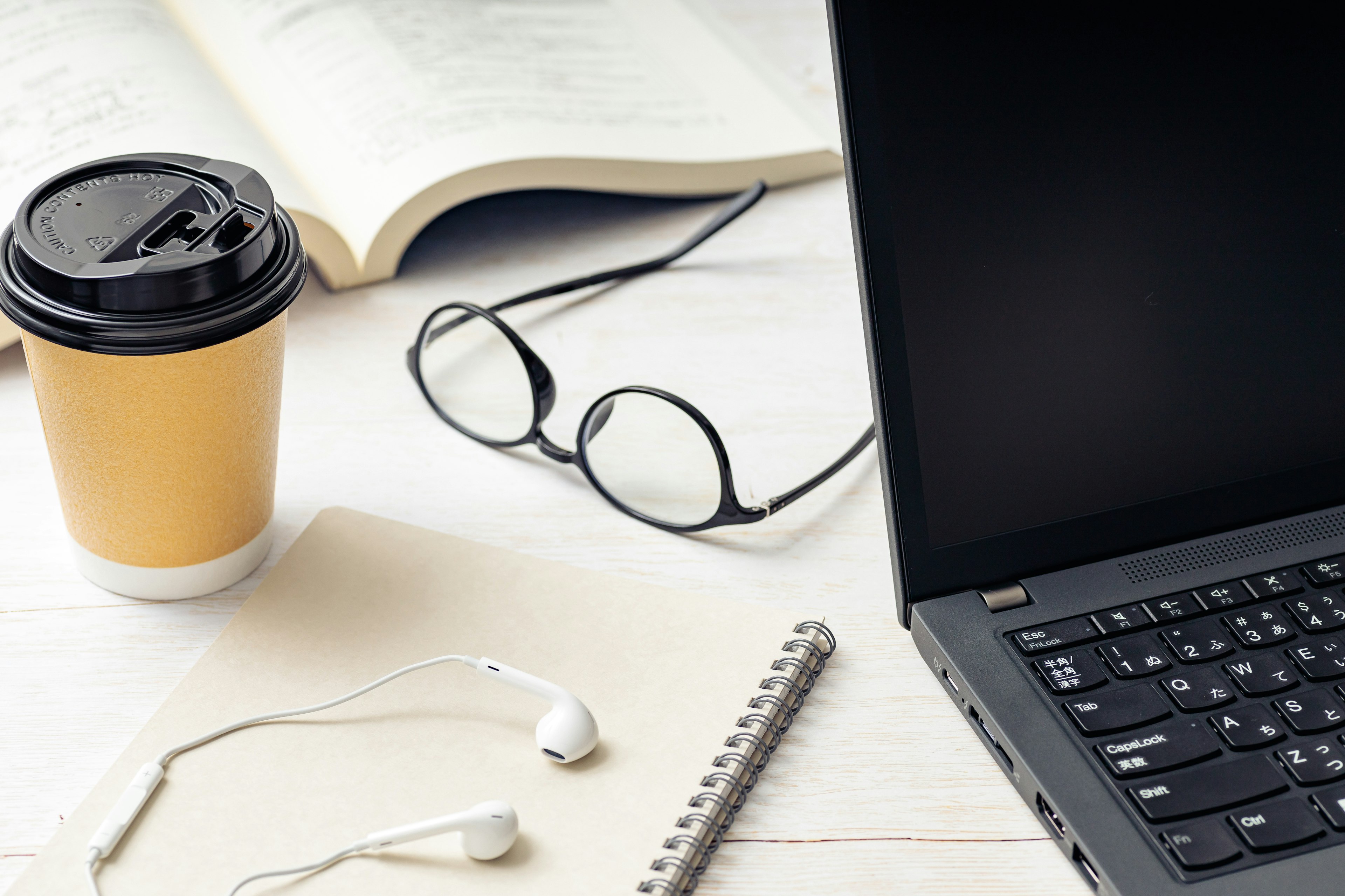 Coffee cup and laptop on desk with a book and glasses