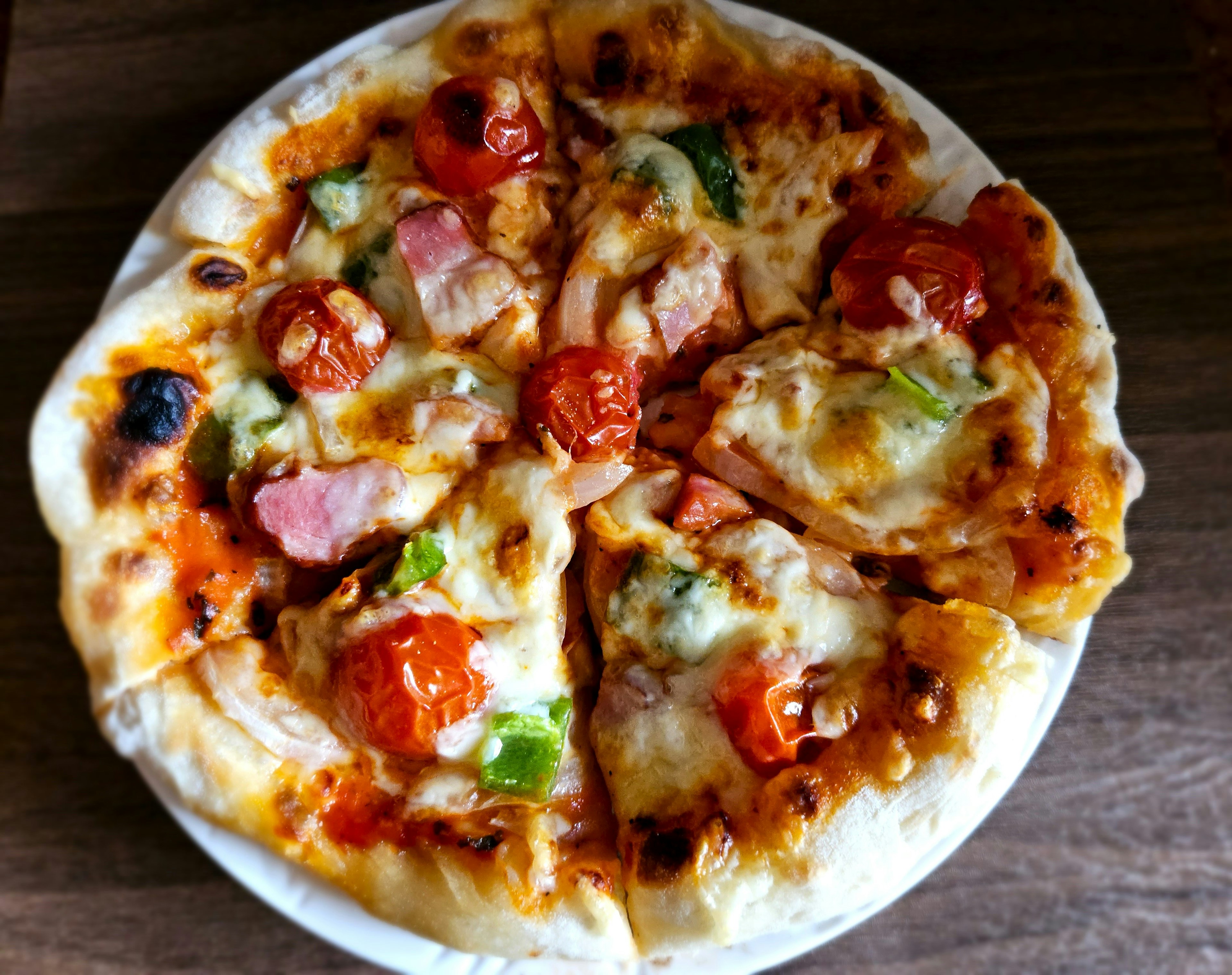 Pizza recién horneada cortada con ingredientes de tomates, tocino y pimientos