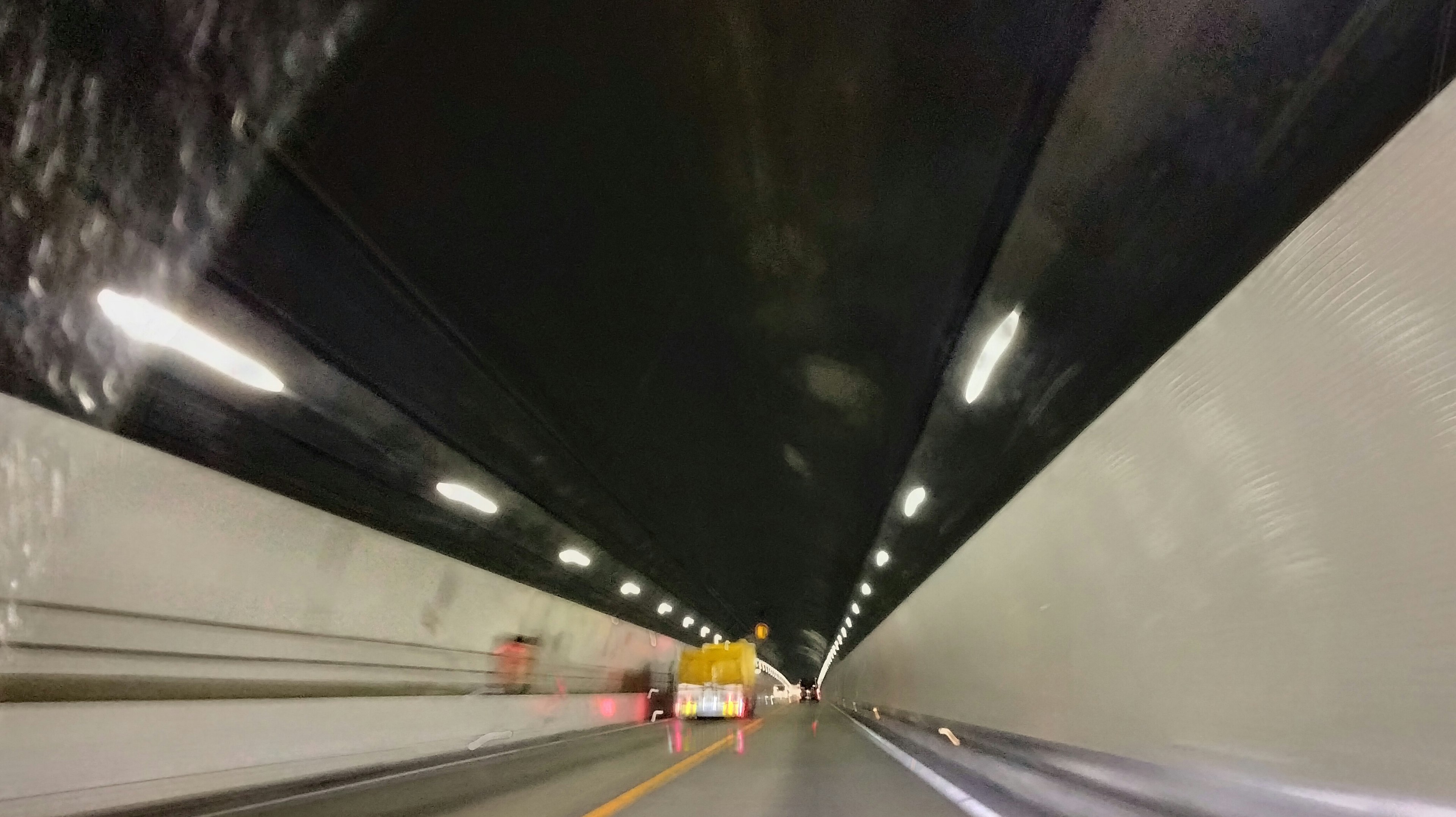 Image from a vehicle's perspective inside a tunnel featuring dark walls and bright lights