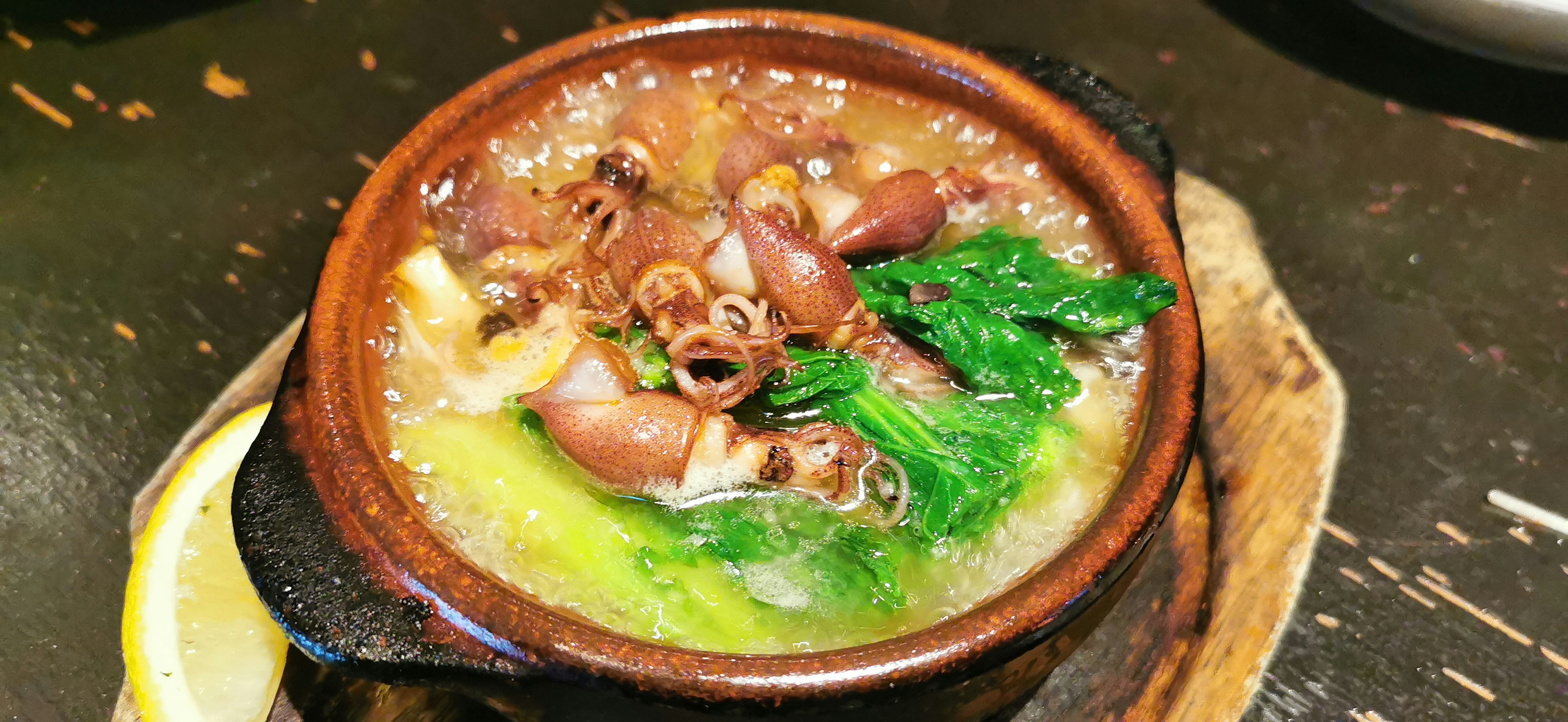 A clay pot filled with soup, greens, and seafood