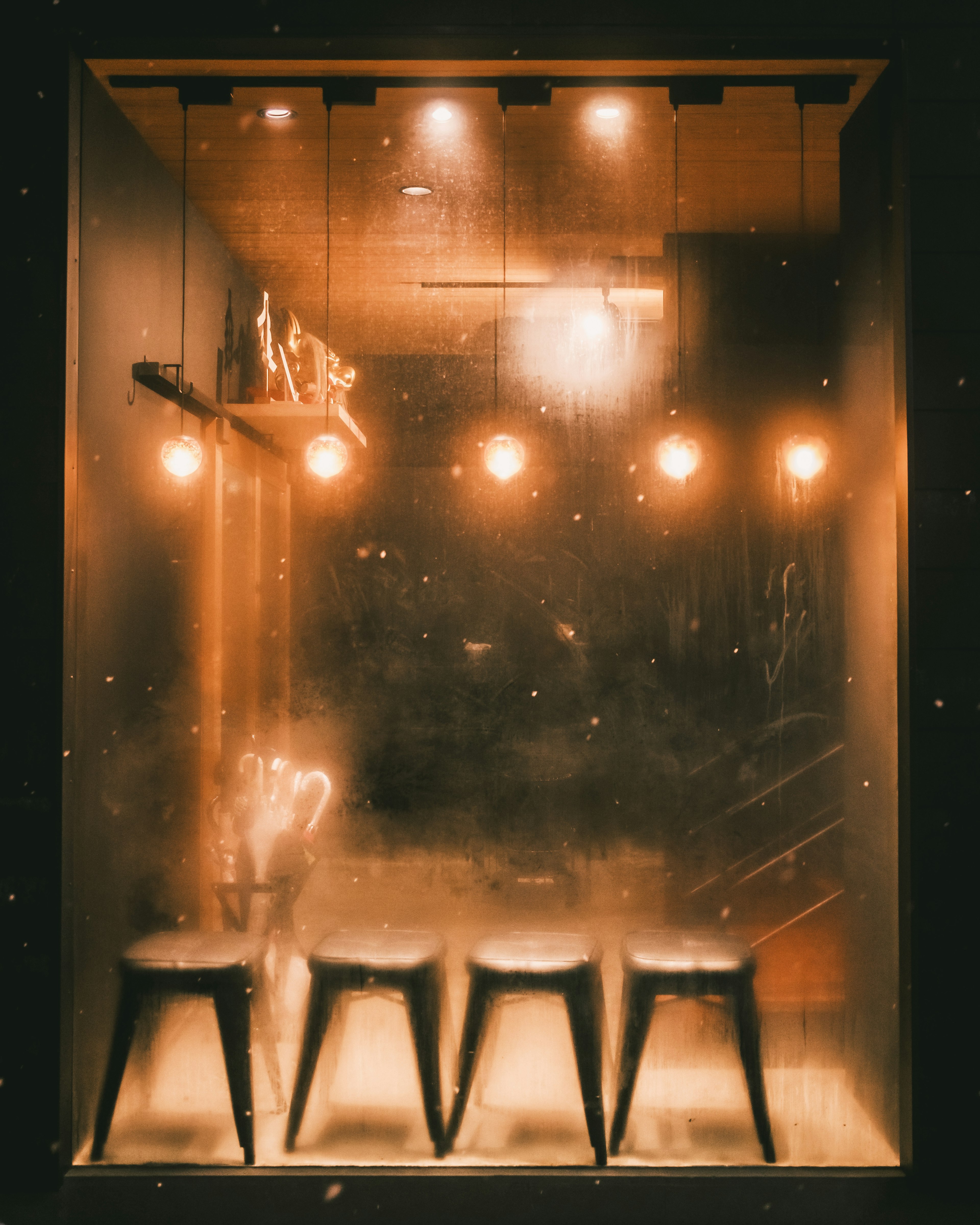 Four stools in front of a fogged window with warm glowing lamps