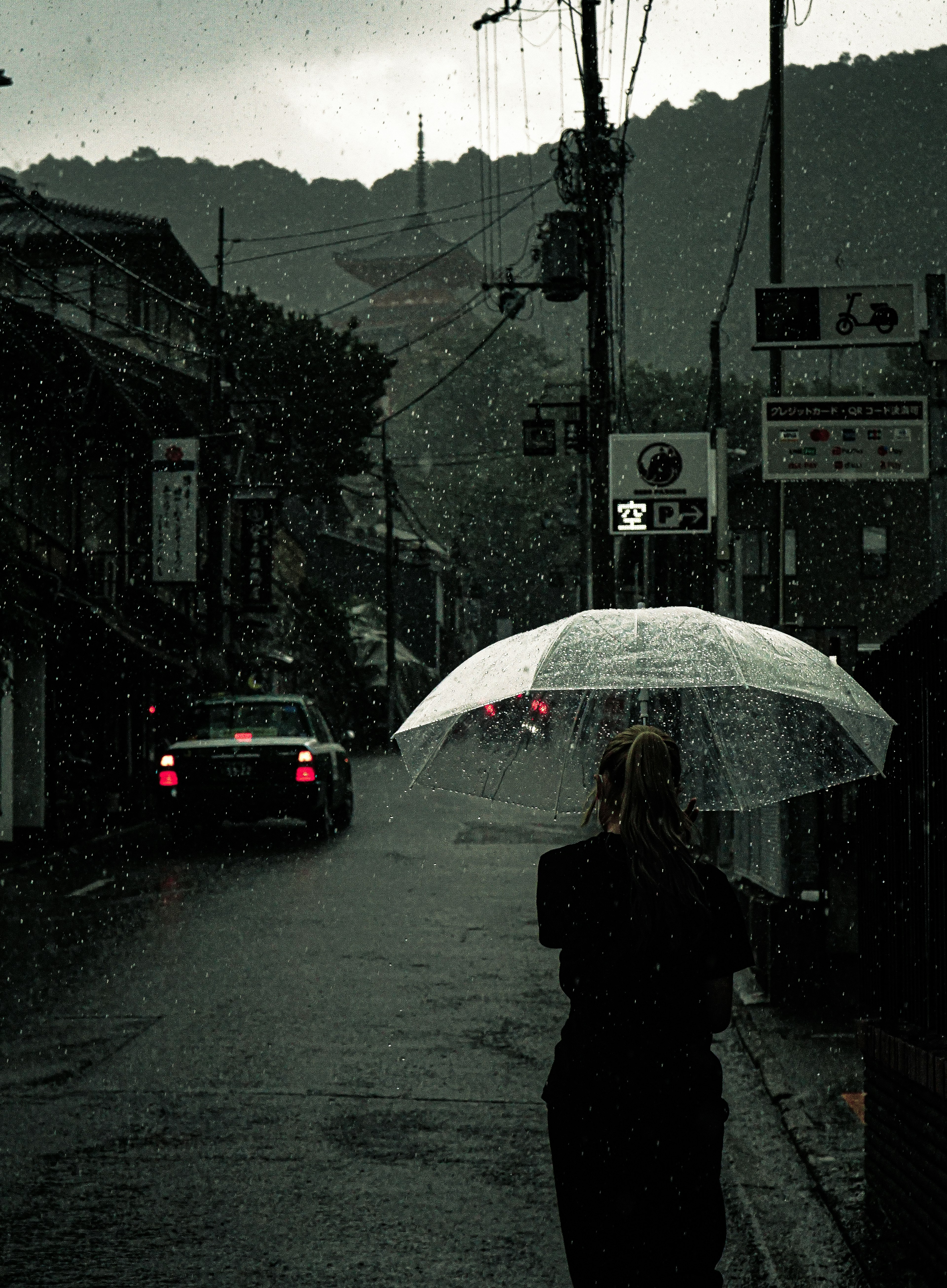 Eine Frau, die mit einem weißen Regenschirm auf einer dunklen Straße im Regen geht