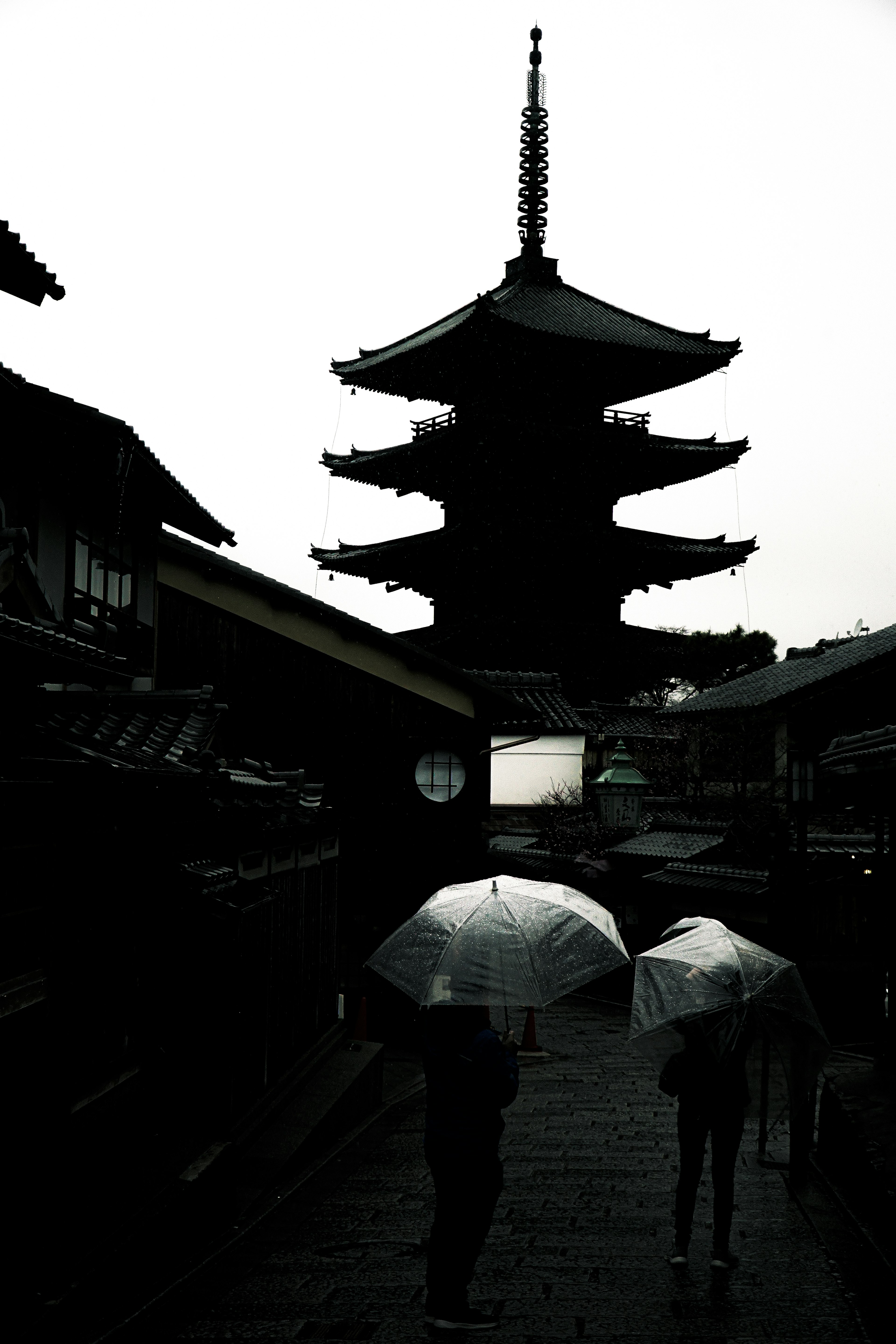 Silhouetted figures with umbrellas walking in front of an ancient five-story pagoda