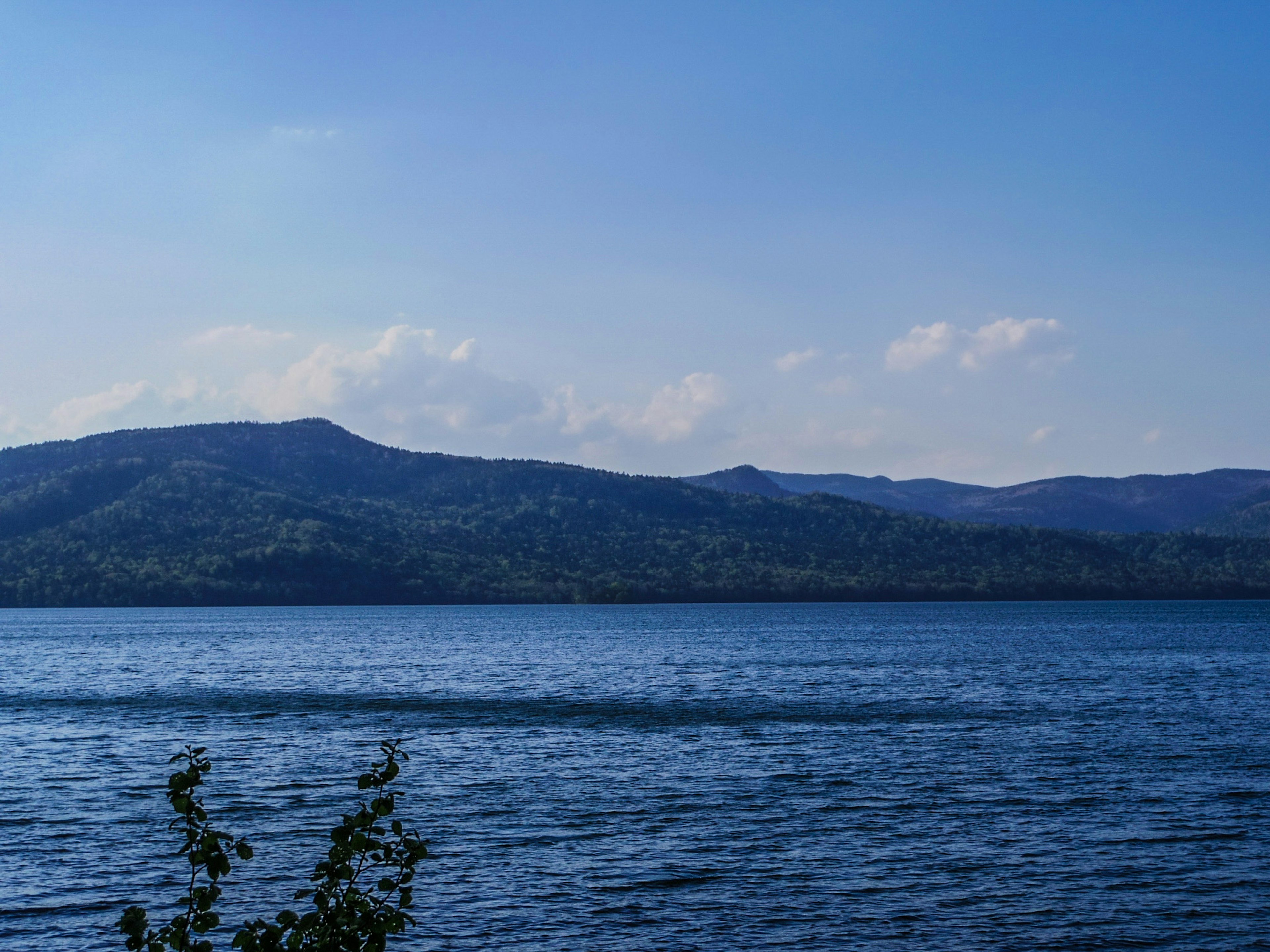 Pemandangan danau yang tenang dengan langit biru dan pegunungan jauh