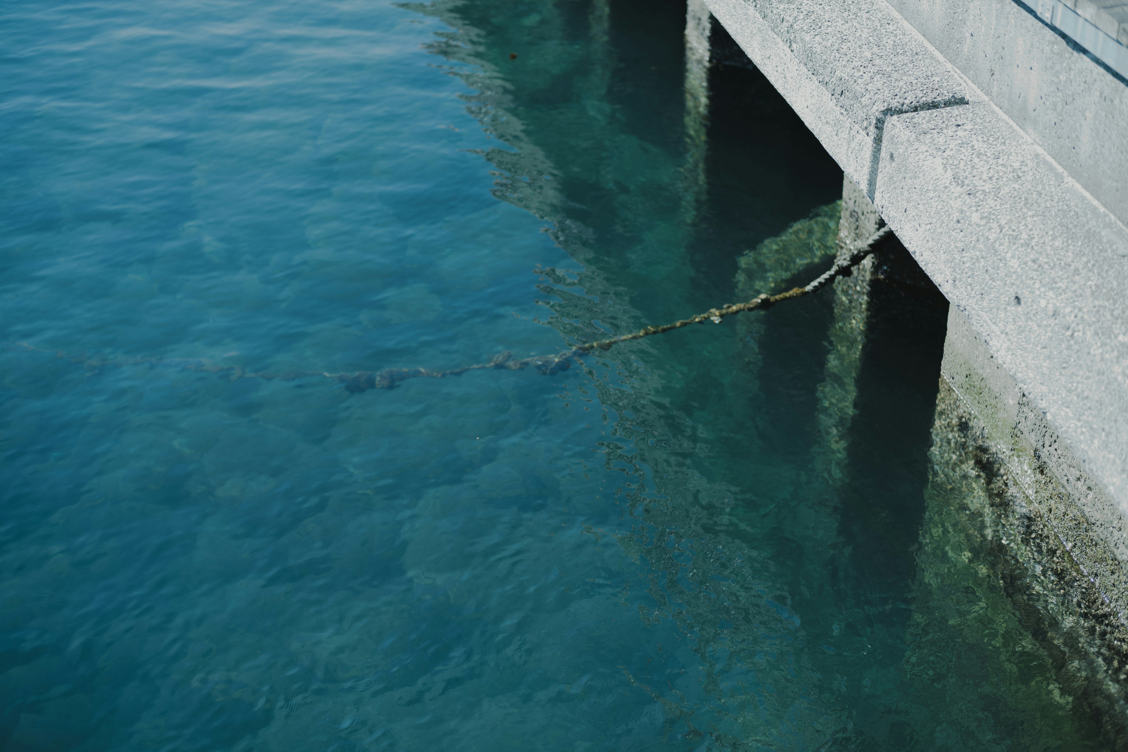 Molo in cemento sopra l'acqua blu con una corda