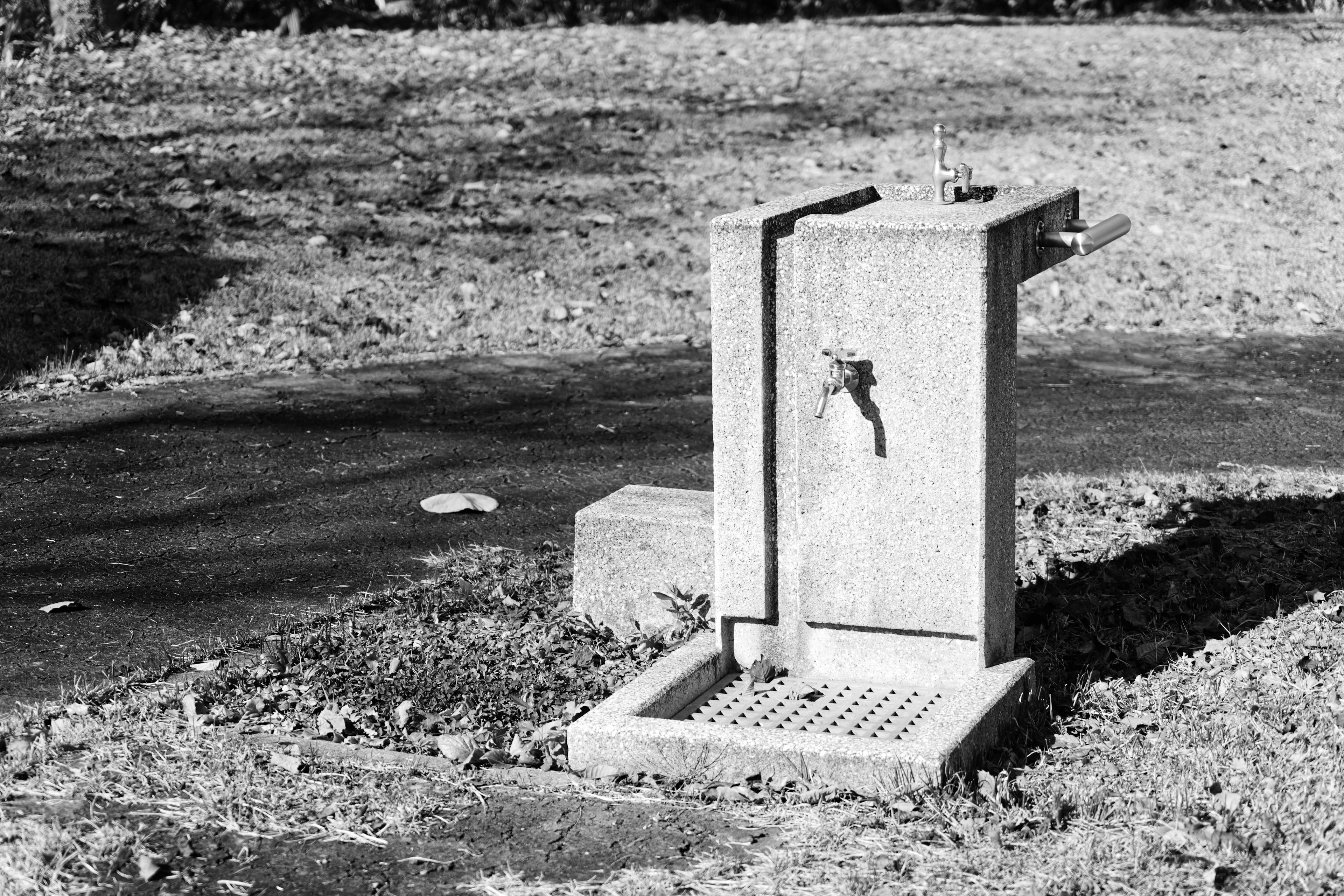 Una fuente de agua en un parque con grava cercana y hierba alrededor