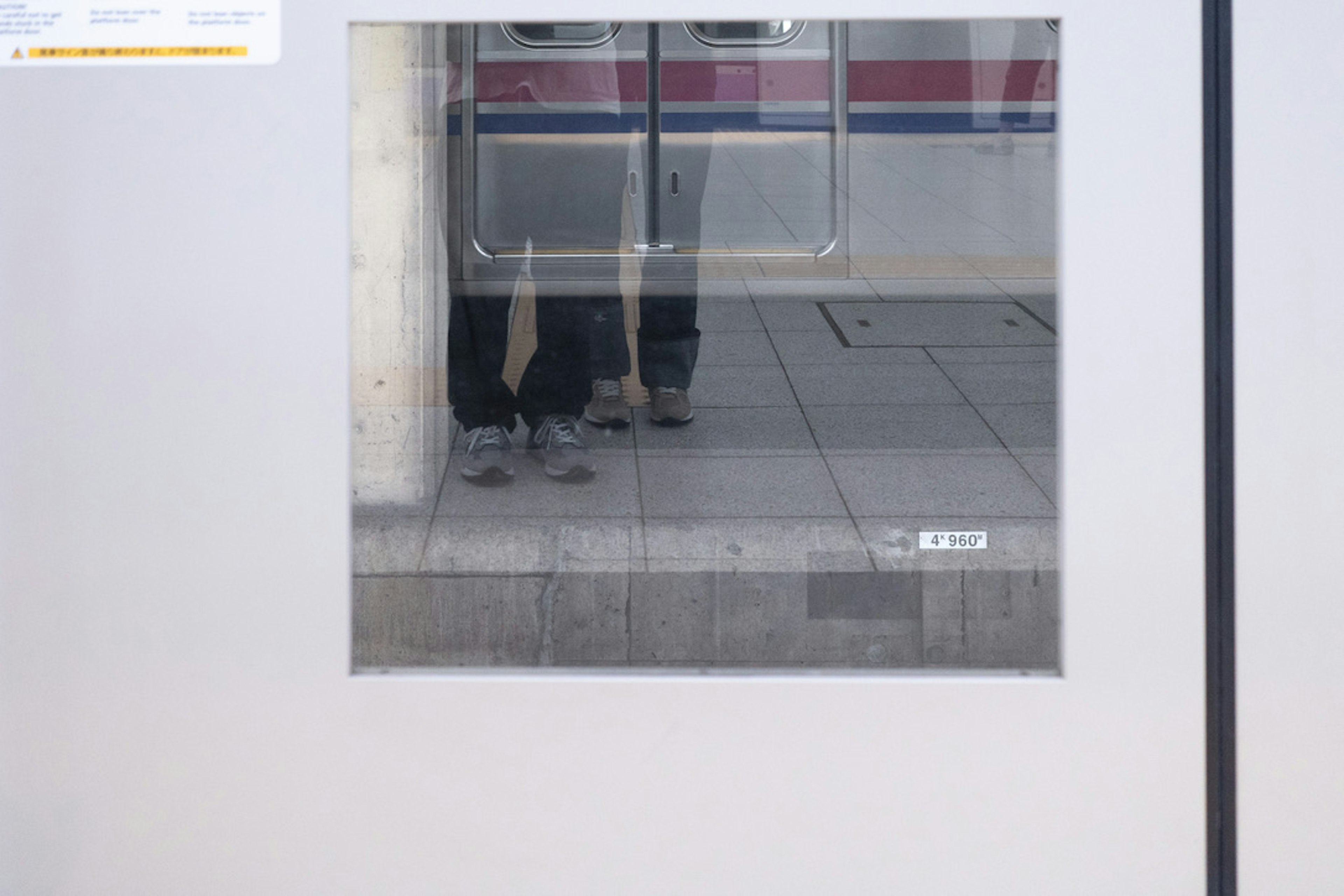 Reflection of people's feet standing on the train platform in the train window