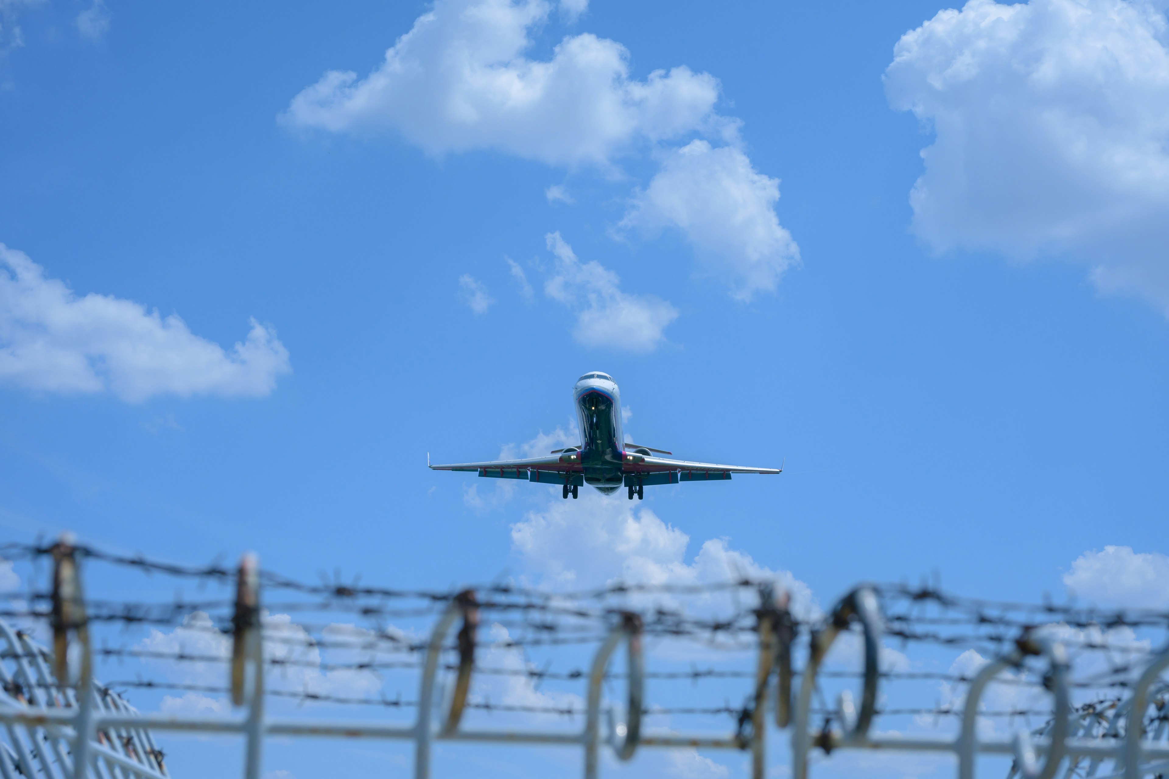 Airplane flying in blue sky above barbed wire fence