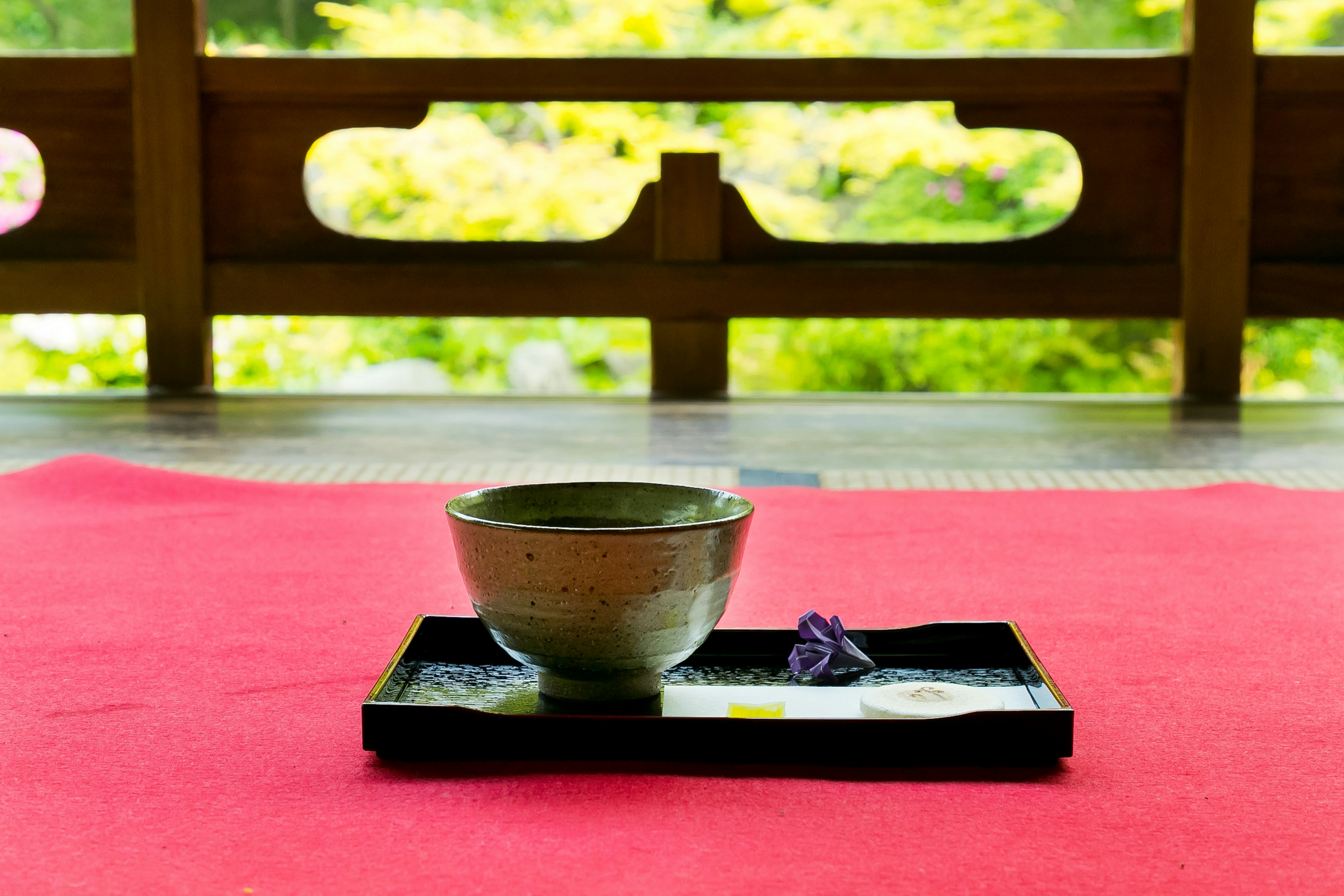 赤い敷物の上に置かれた茶碗と黒いトレイの前景 緑の自然の背景