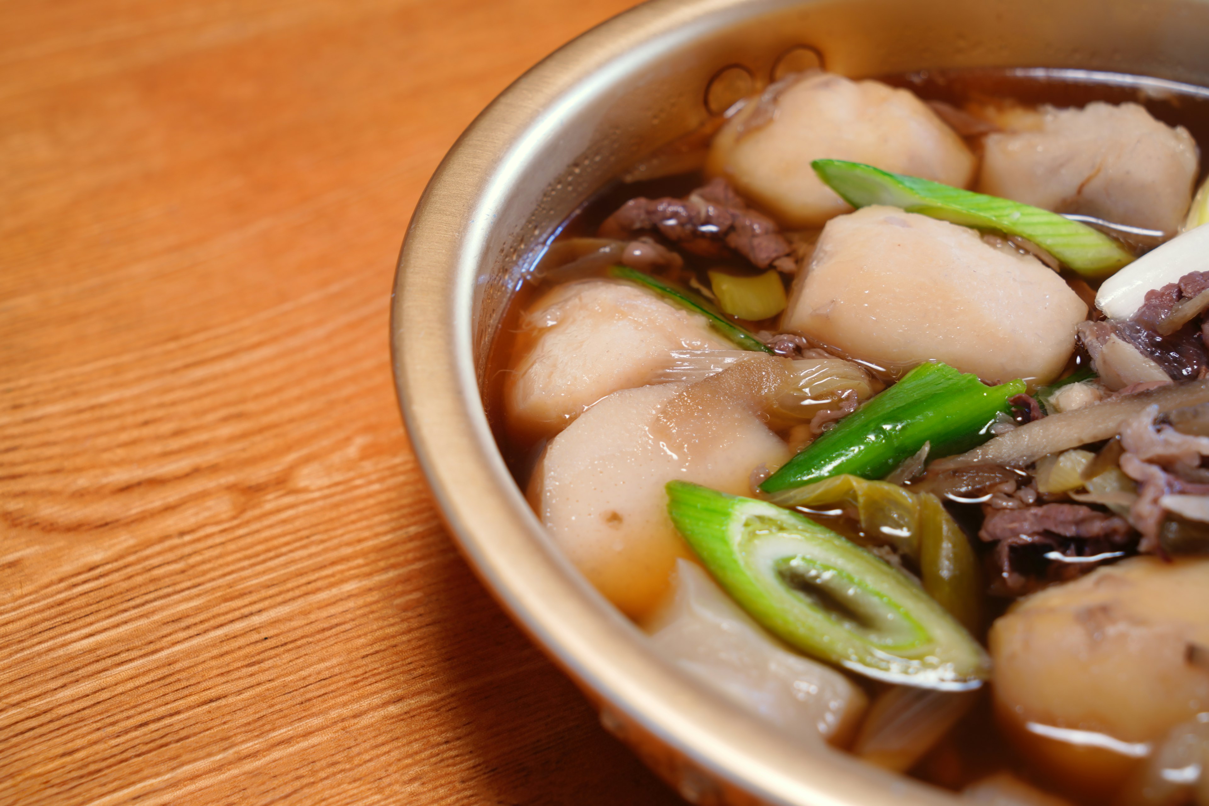 A bowl of soup featuring white dumplings and green onions