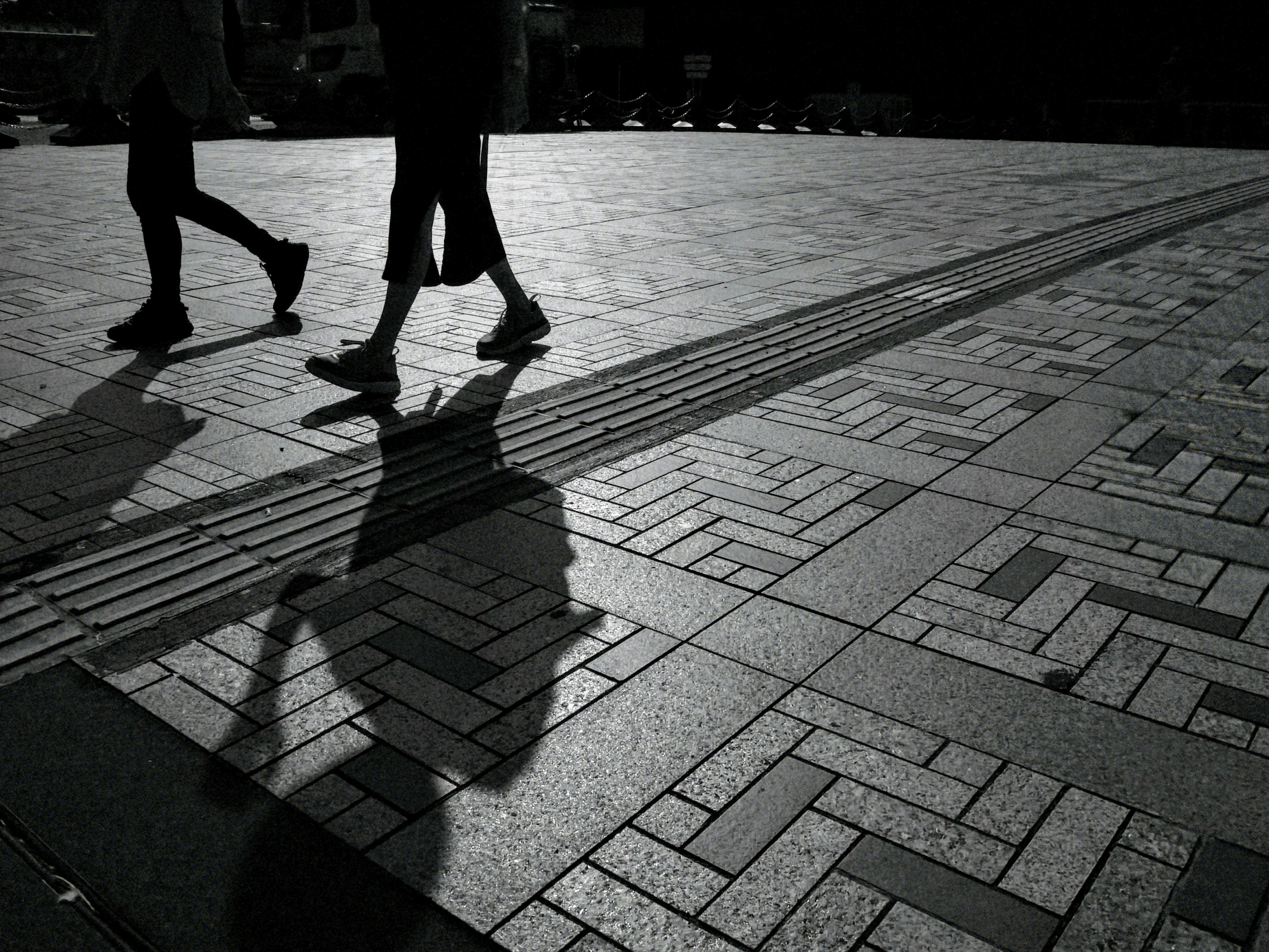 Silhouettes of people walking on patterned pavement