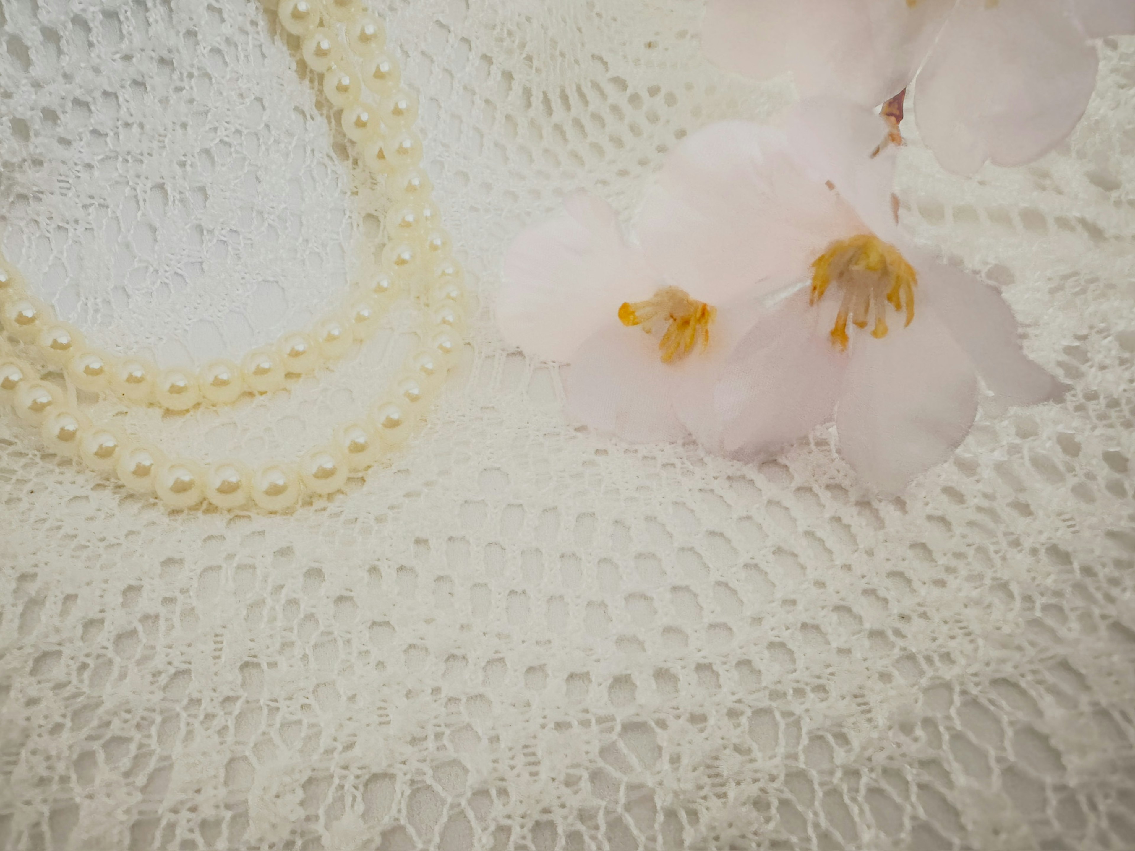 A pearl necklace and soft pink flowers on a white lace tablecloth