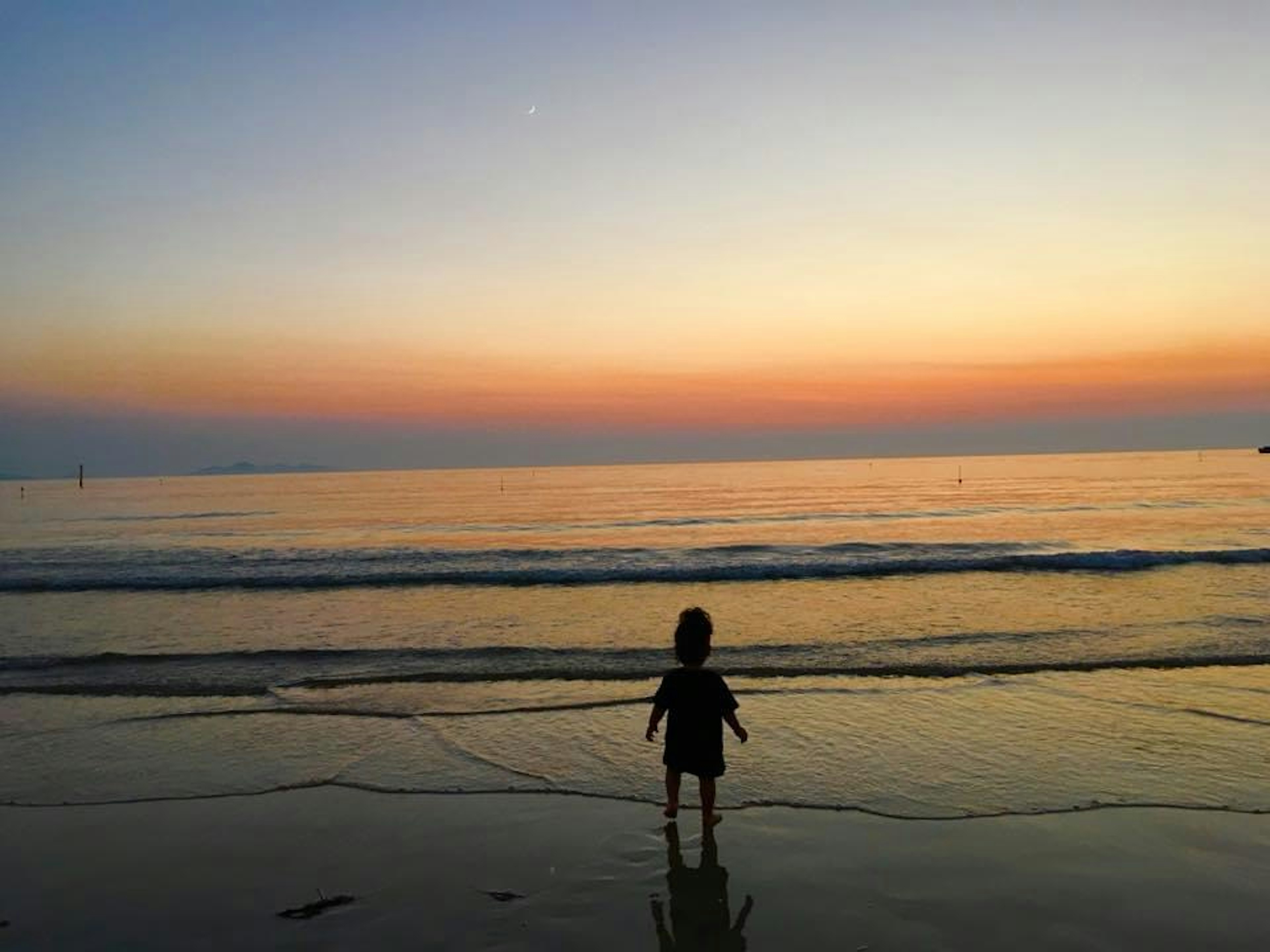 Silhouette eines Kindes, das am Strand bei Sonnenuntergang spielt