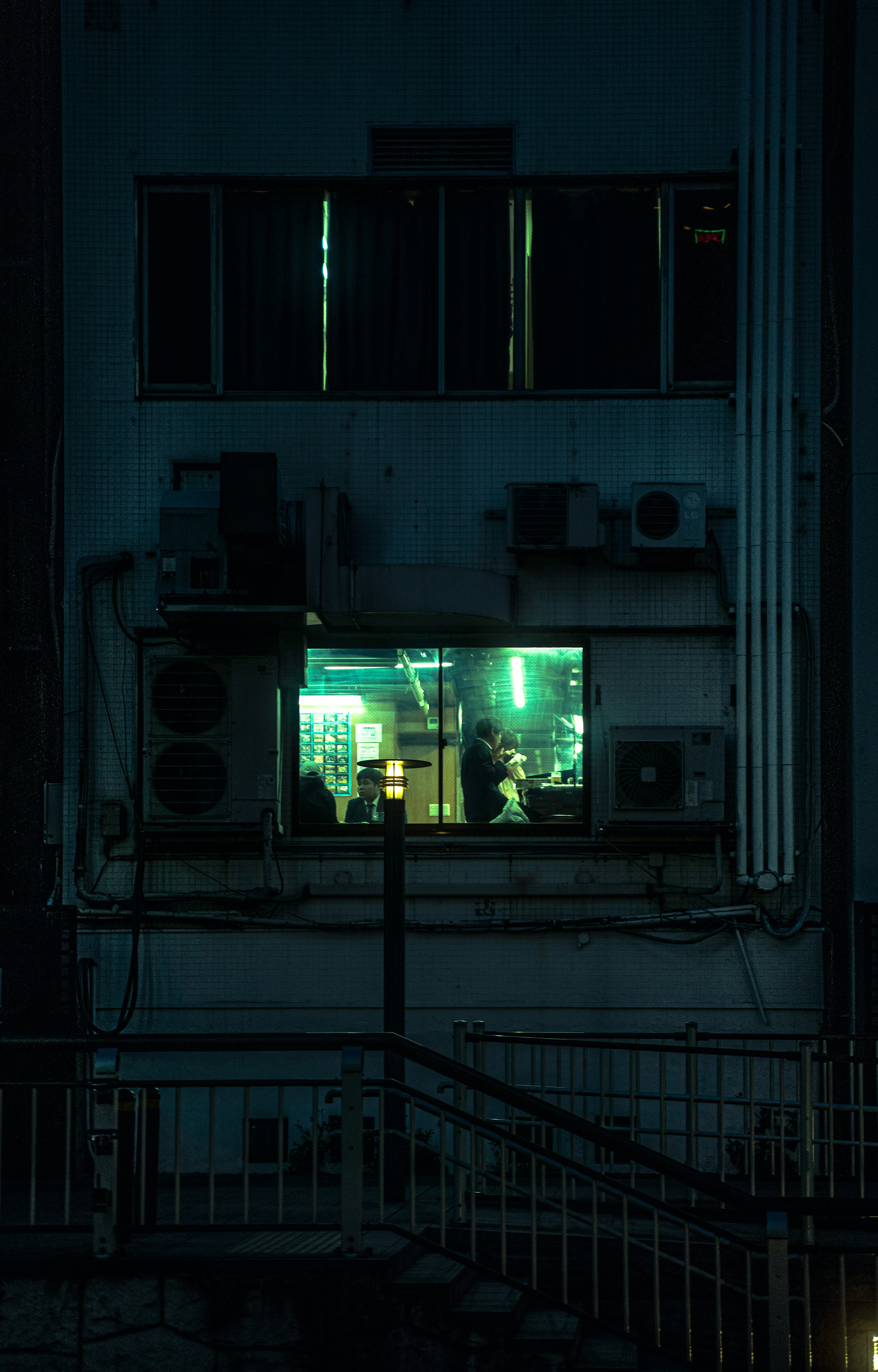 Vista esterna di un edificio con una finestra verde illuminata in un ambiente scuro