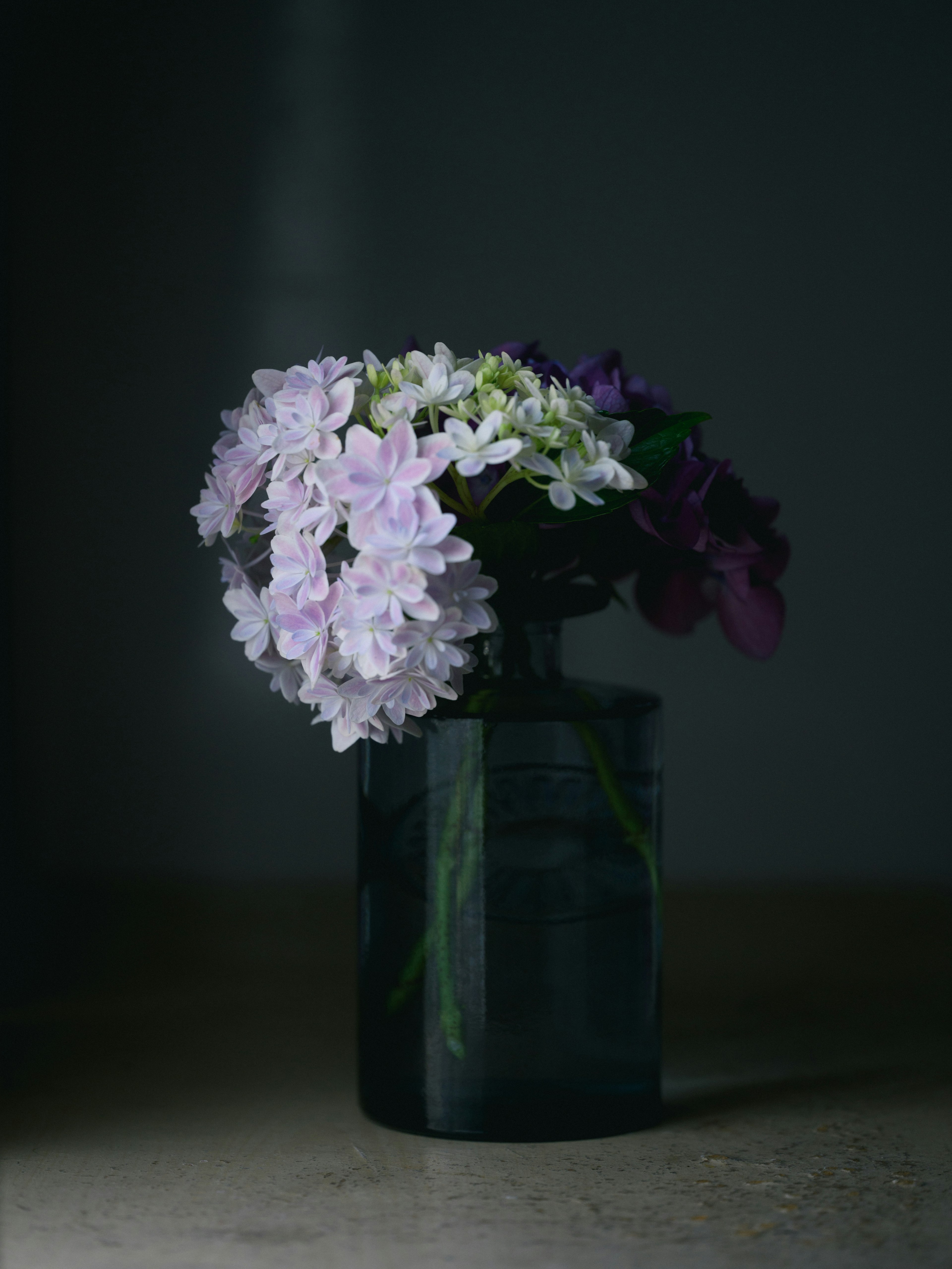 A bouquet of purple and white flowers in a dark vase against a dim background