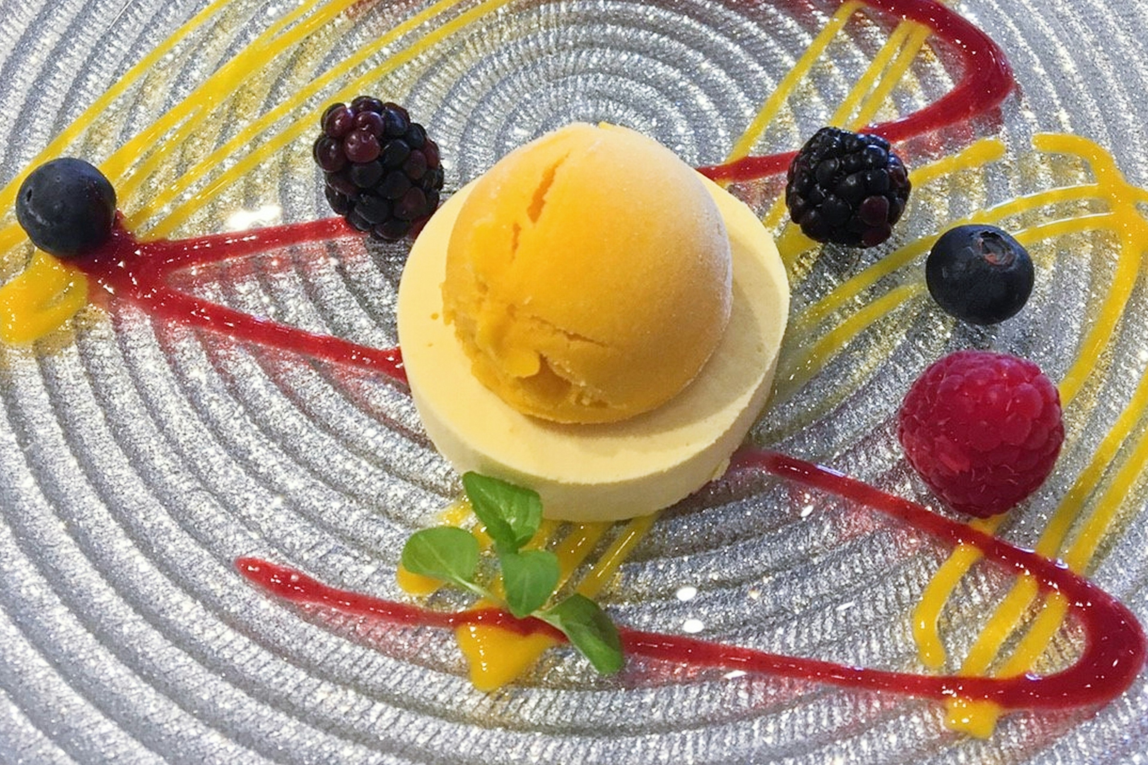 Gelato giallo con salsa di frutta su piatto artistico