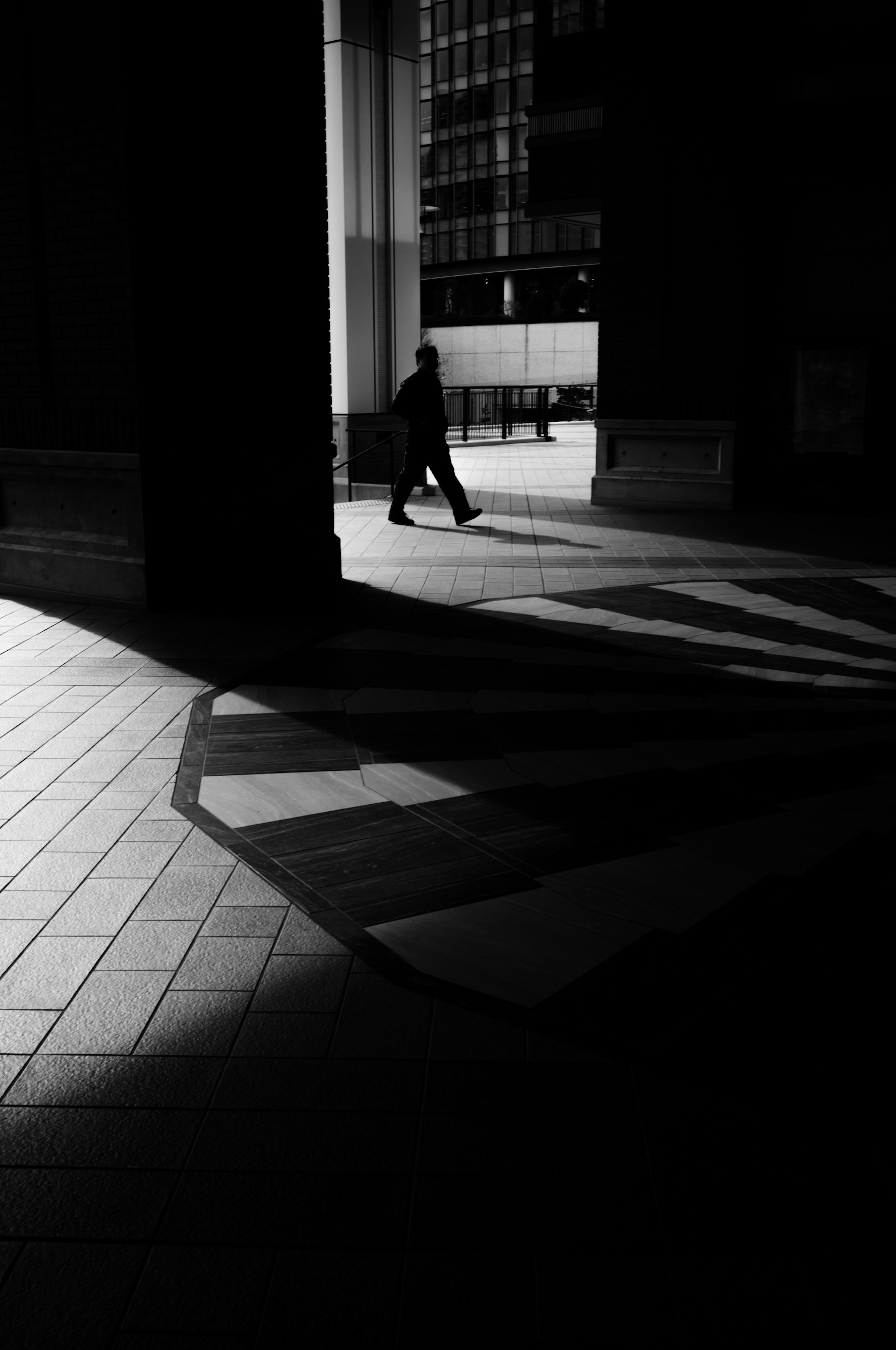 Escena urbana en blanco y negro con una persona caminando en la sombra