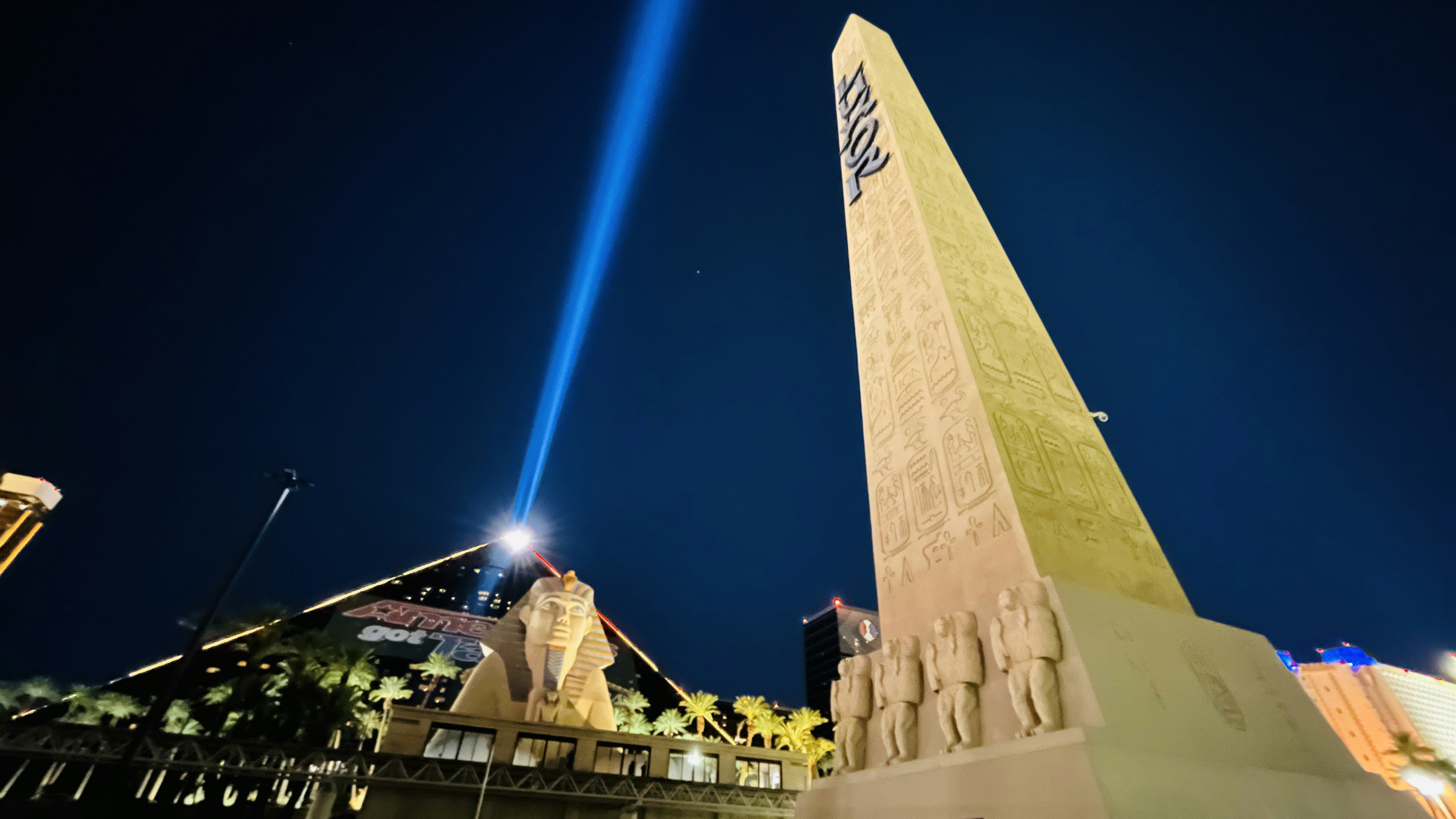 Vista nocturna de una pirámide y un obelisco con un haz de luz iluminando hacia arriba