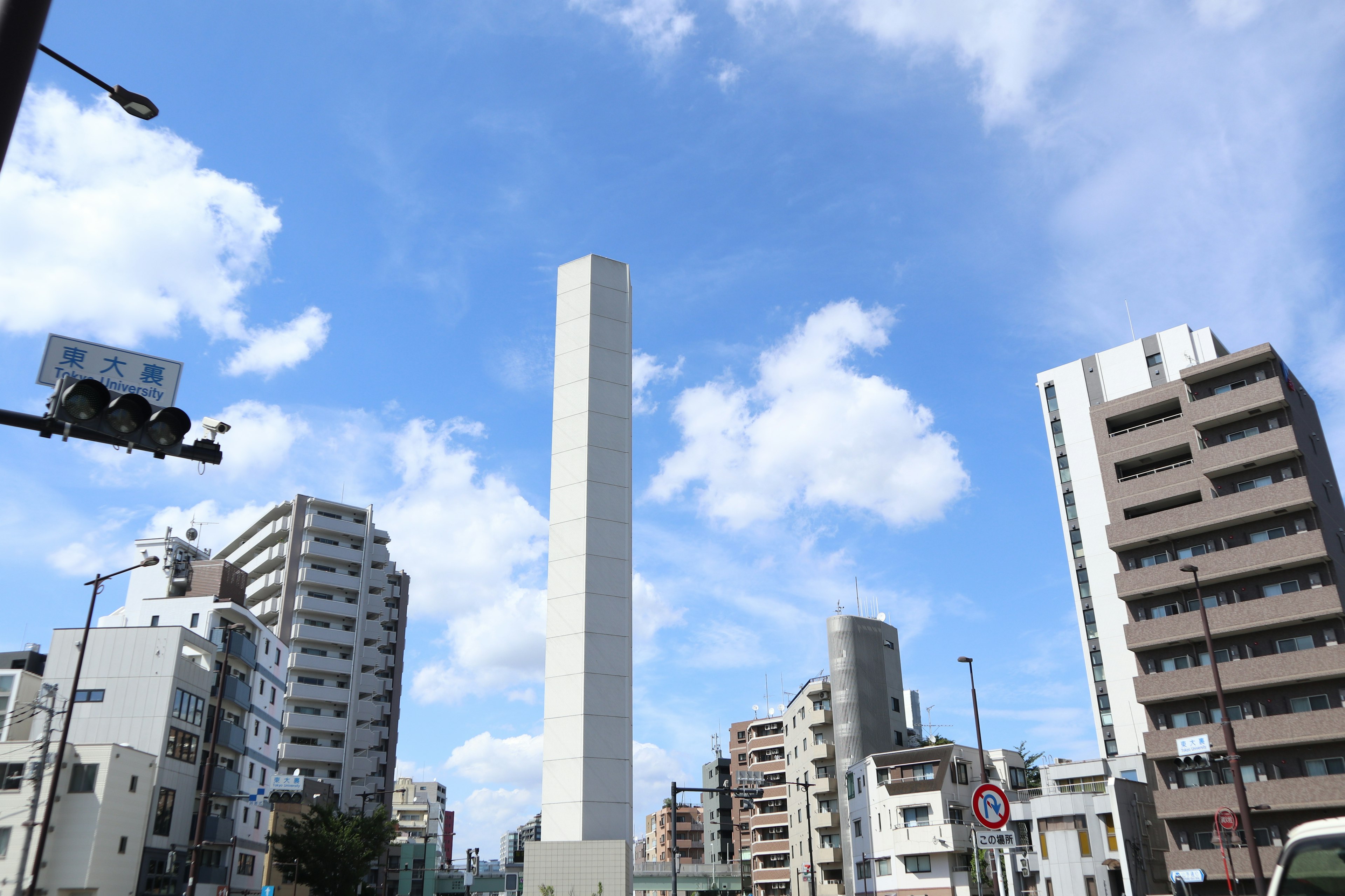 Menara beton tinggi di bawah langit biru dikelilingi oleh gedung-gedung tinggi