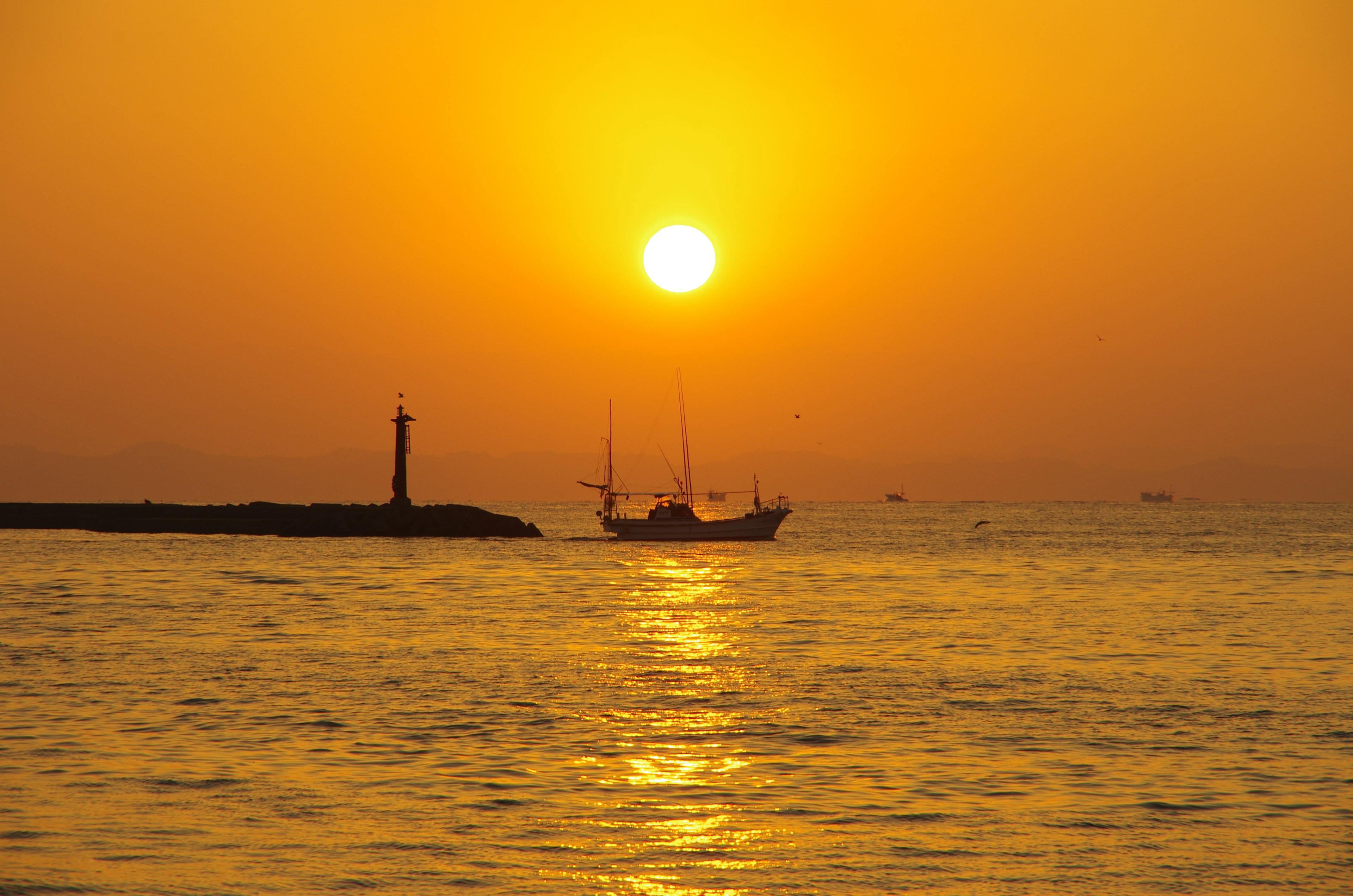 海上的美丽日落，远处有一艘船和一座灯塔