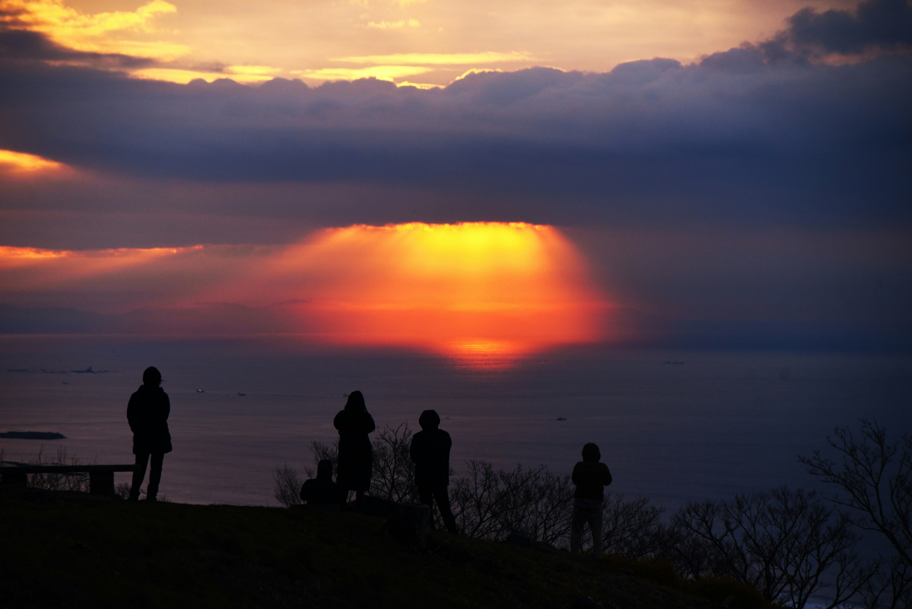 Silhouetten von Menschen, die den Sonnenuntergang über dem Meer mit lebhaften Farben am Himmel beobachten