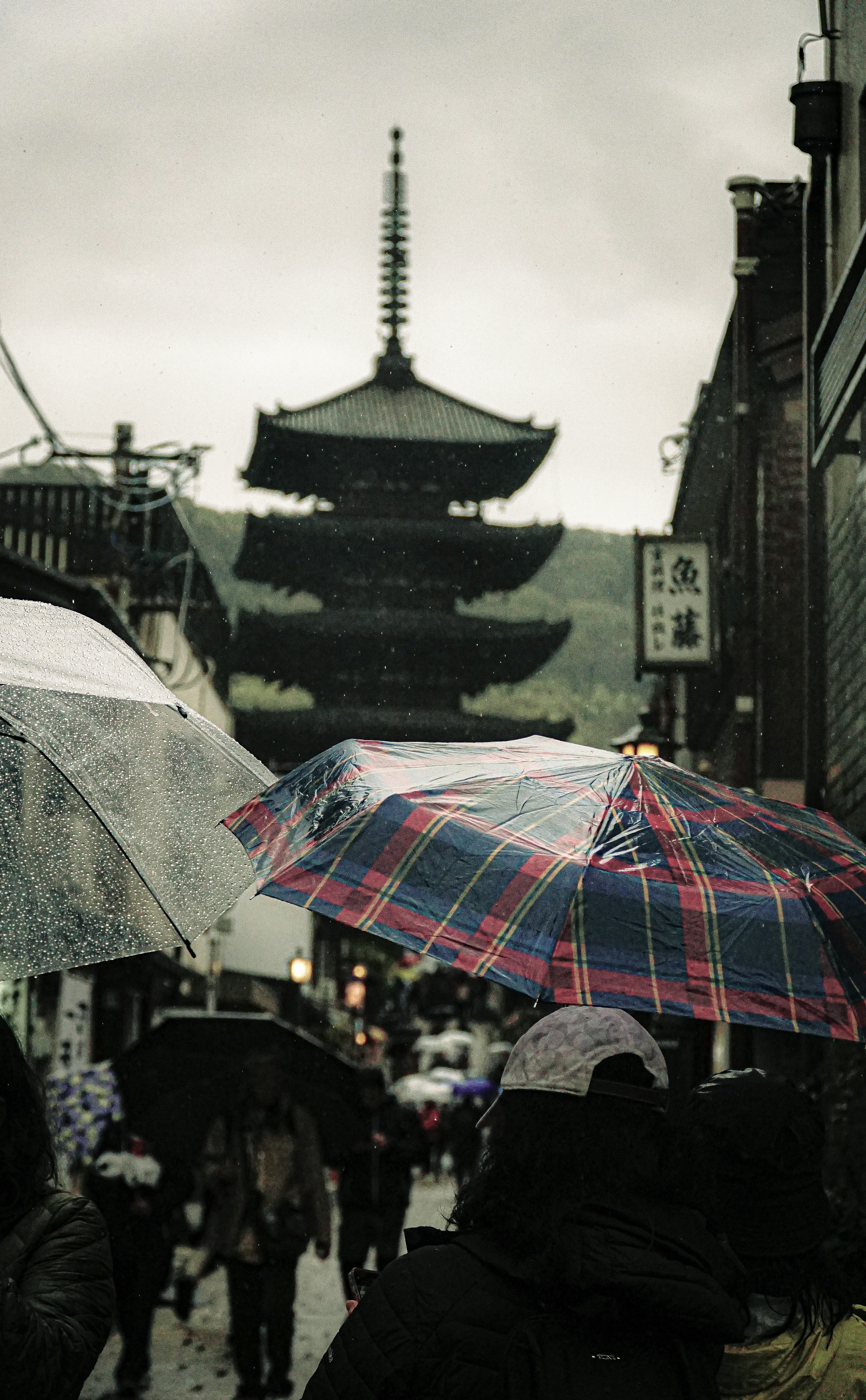 雨の中、五重塔が見える街並みと傘を持つ人々