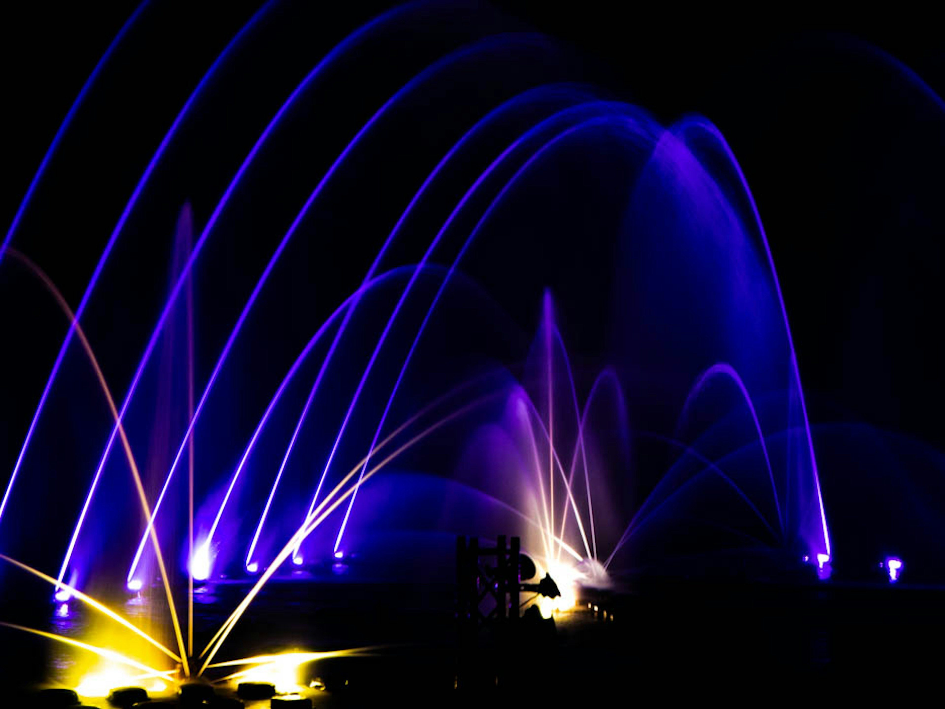 Nachtliche Springbrunnen-Show mit lila Strahlen, die Wasserbögen bilden