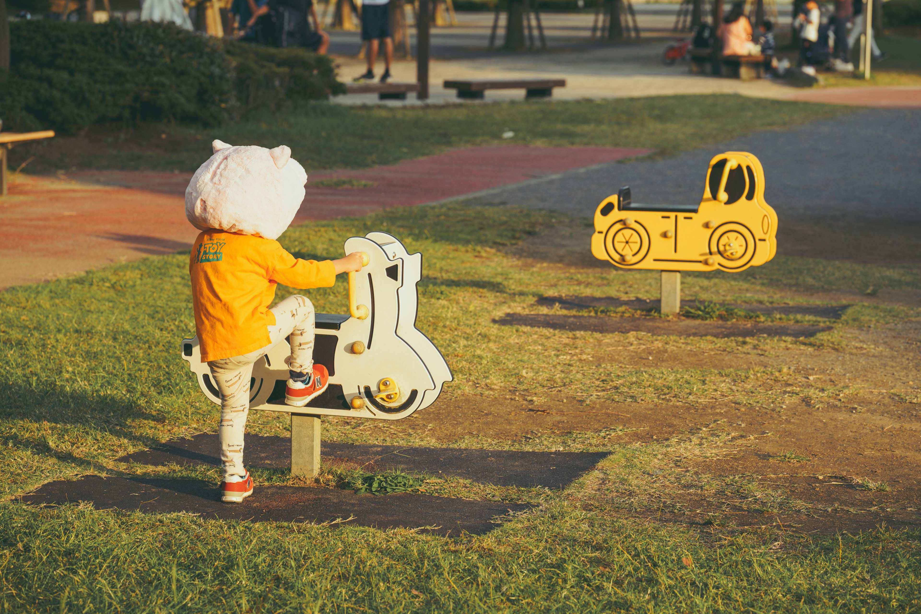 Enfant jouant sur un équipement de jeu en forme de scooter avec un équipement en forme de voiture jaune à proximité